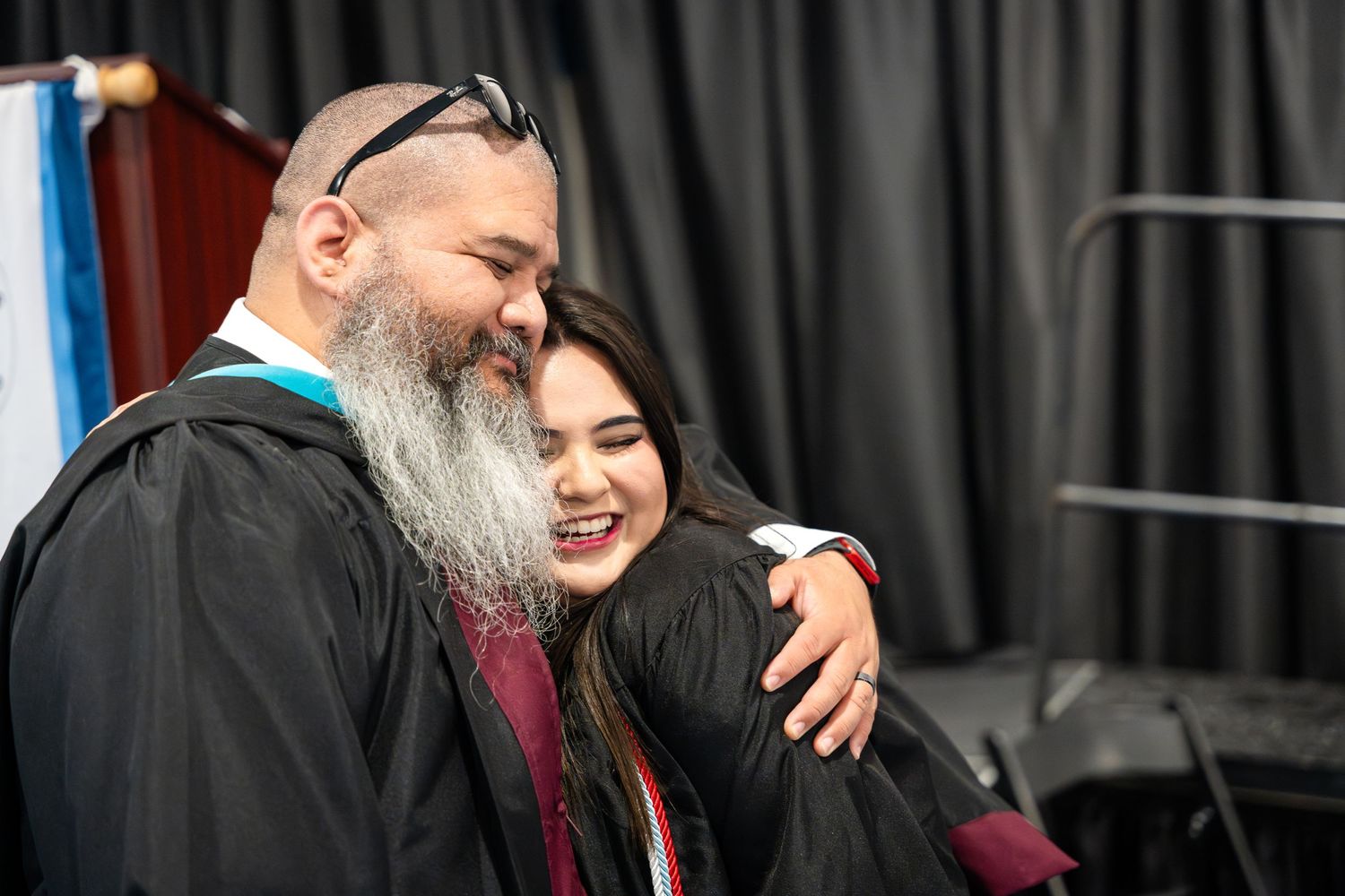 A touching moment shared during a graduation ceremony against a black curtain backdrop.
