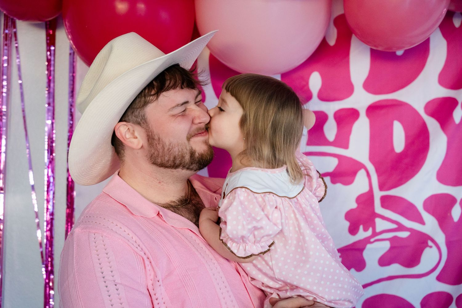 A sweet moment captured against a pink balloon backdrop with hearts and frill decorations.