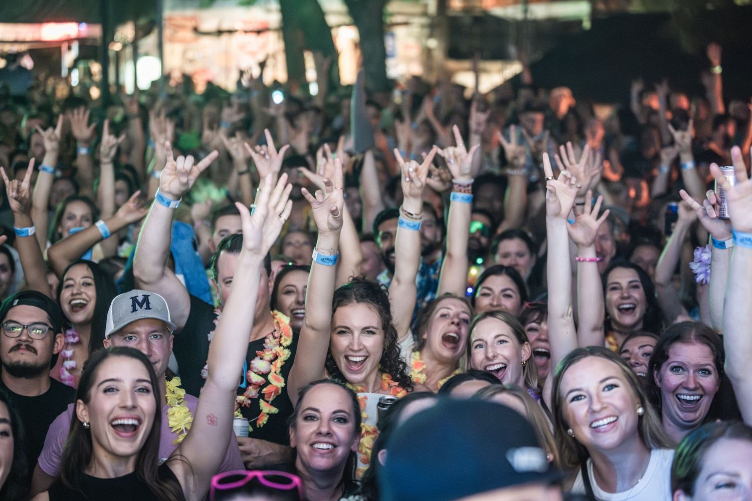 Enthusiastic crowd with raised hands cheering at an outdoor music festival.
