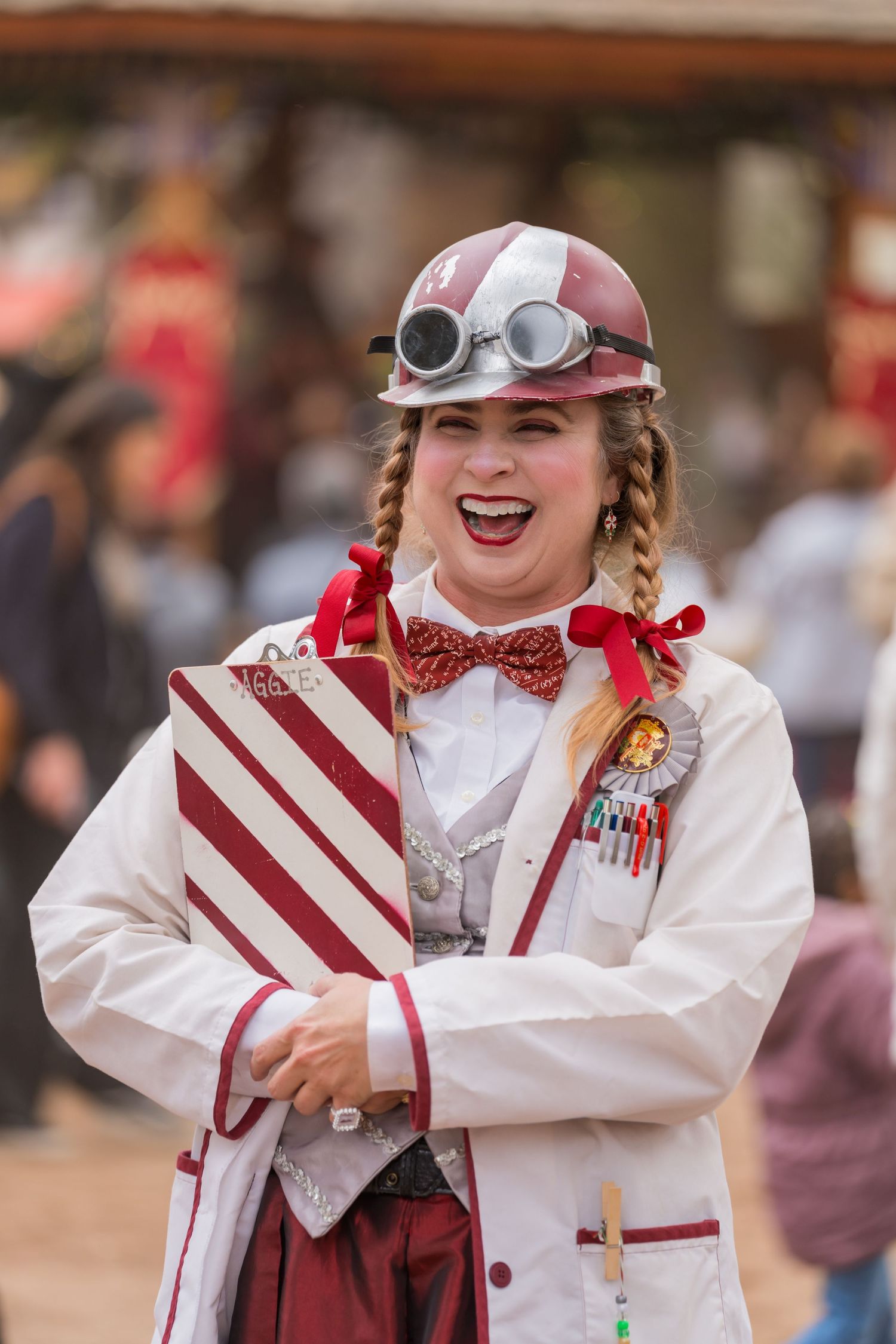 Performer in candy-striped costume and steampunk goggles smiles at renaissance festival.