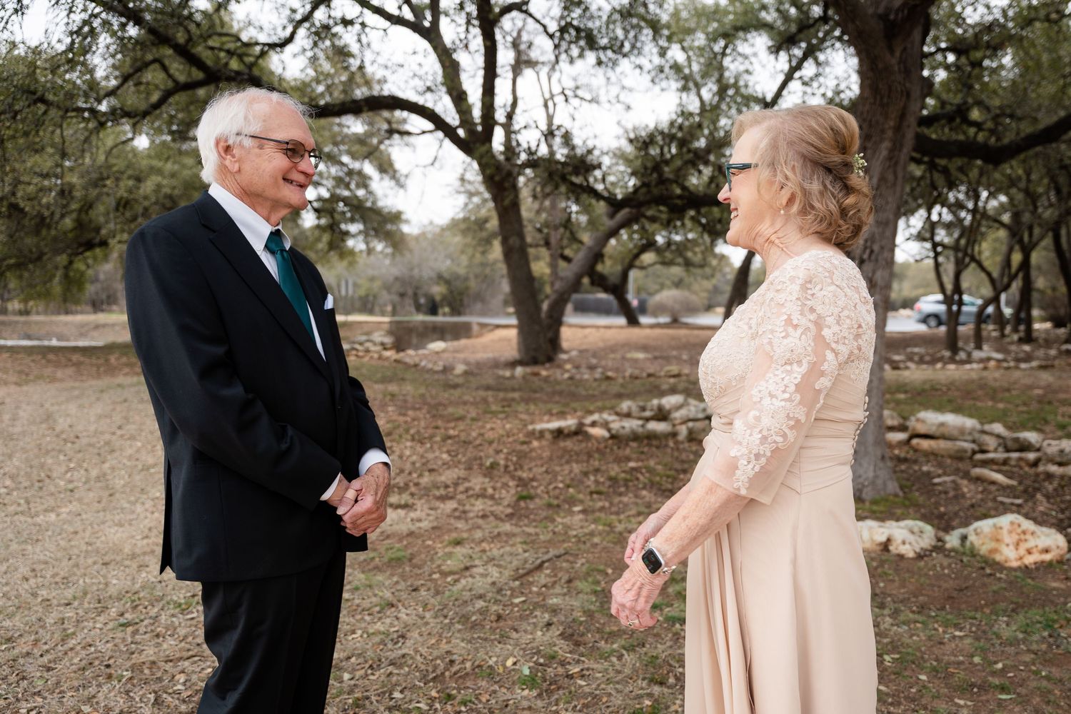 Two people share an intimate moment outdoors under oak trees during a romantic ceremony in muted tones.