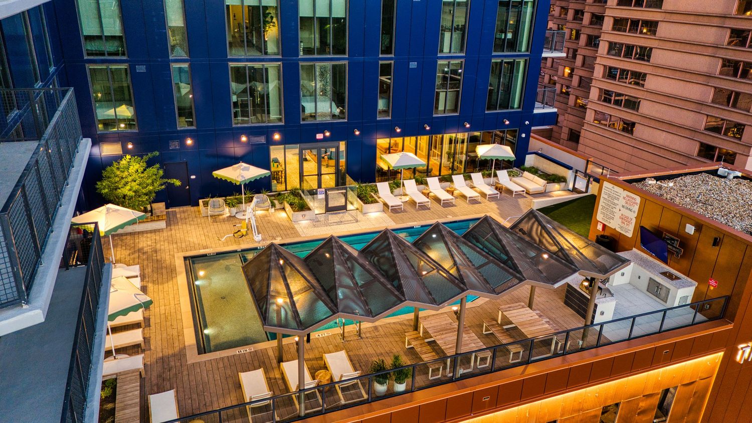 Twilight aerial view of modern apartment building's rooftop amenity deck with pool and lounging areas.