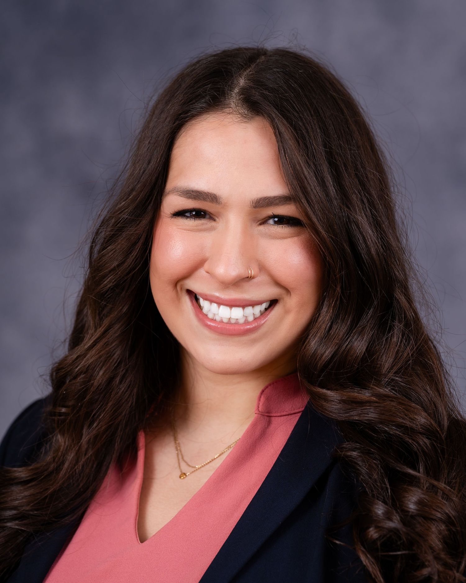 Professional headshot of woman in business attire smiling against gray background.