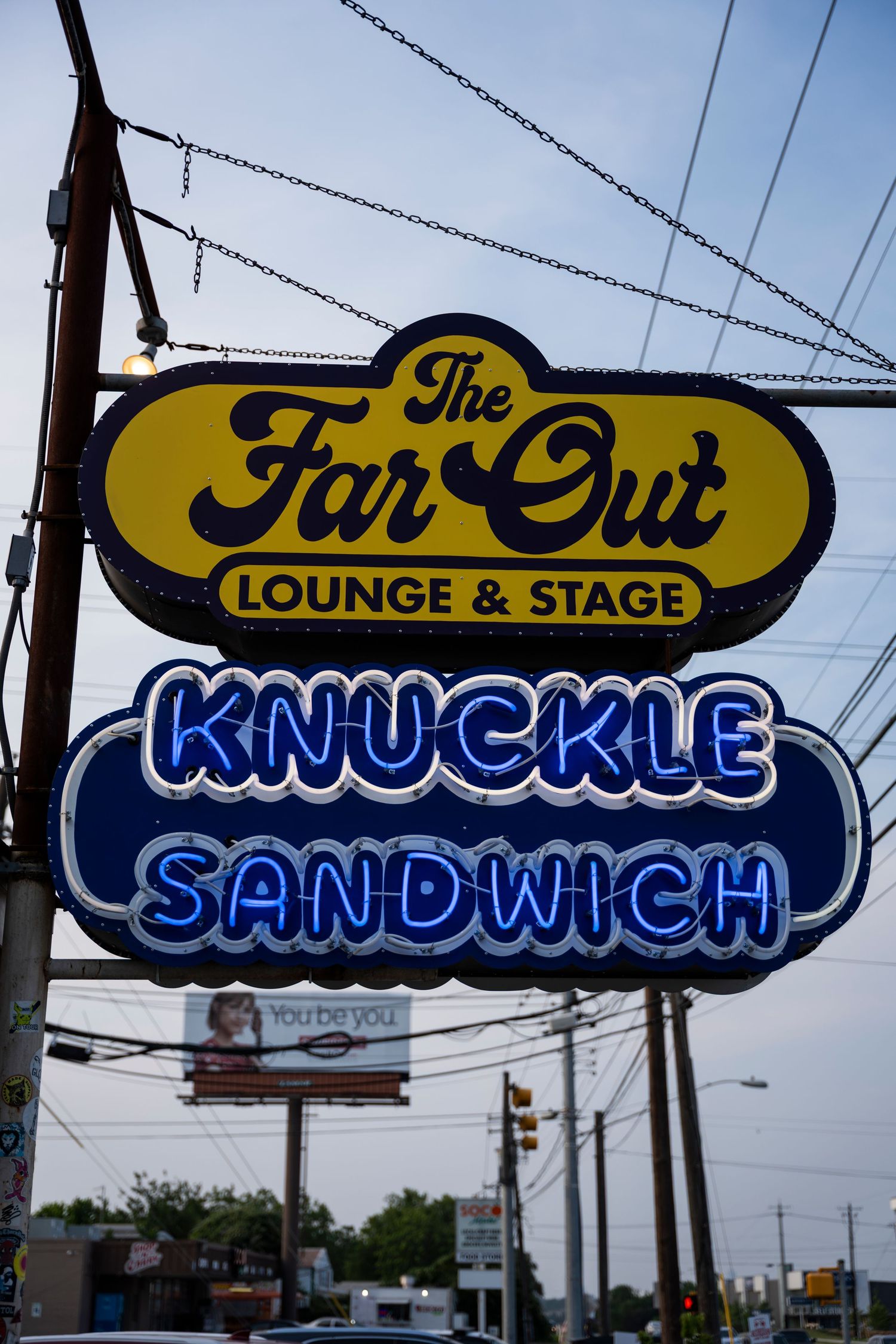 Vintage illuminated signage outside 'The Far Out Lounge & Stage' bar shows yellow and blue neon lettering against dusk sky.