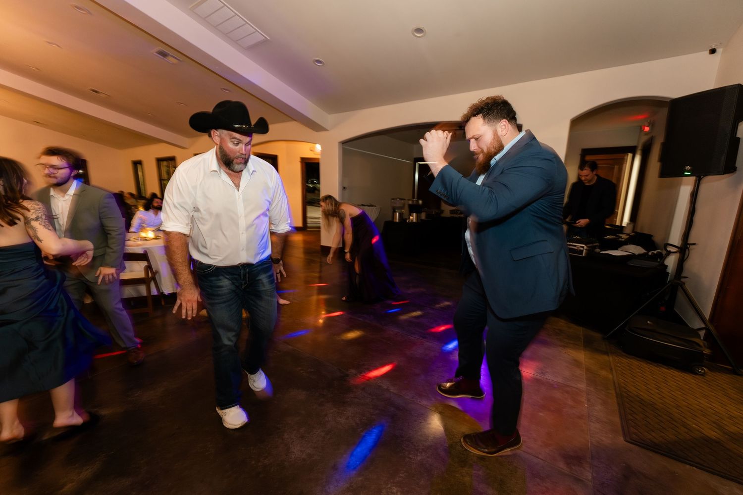 Two men dancing energetically at an indoor party with colorful DJ lights on the dance floor.