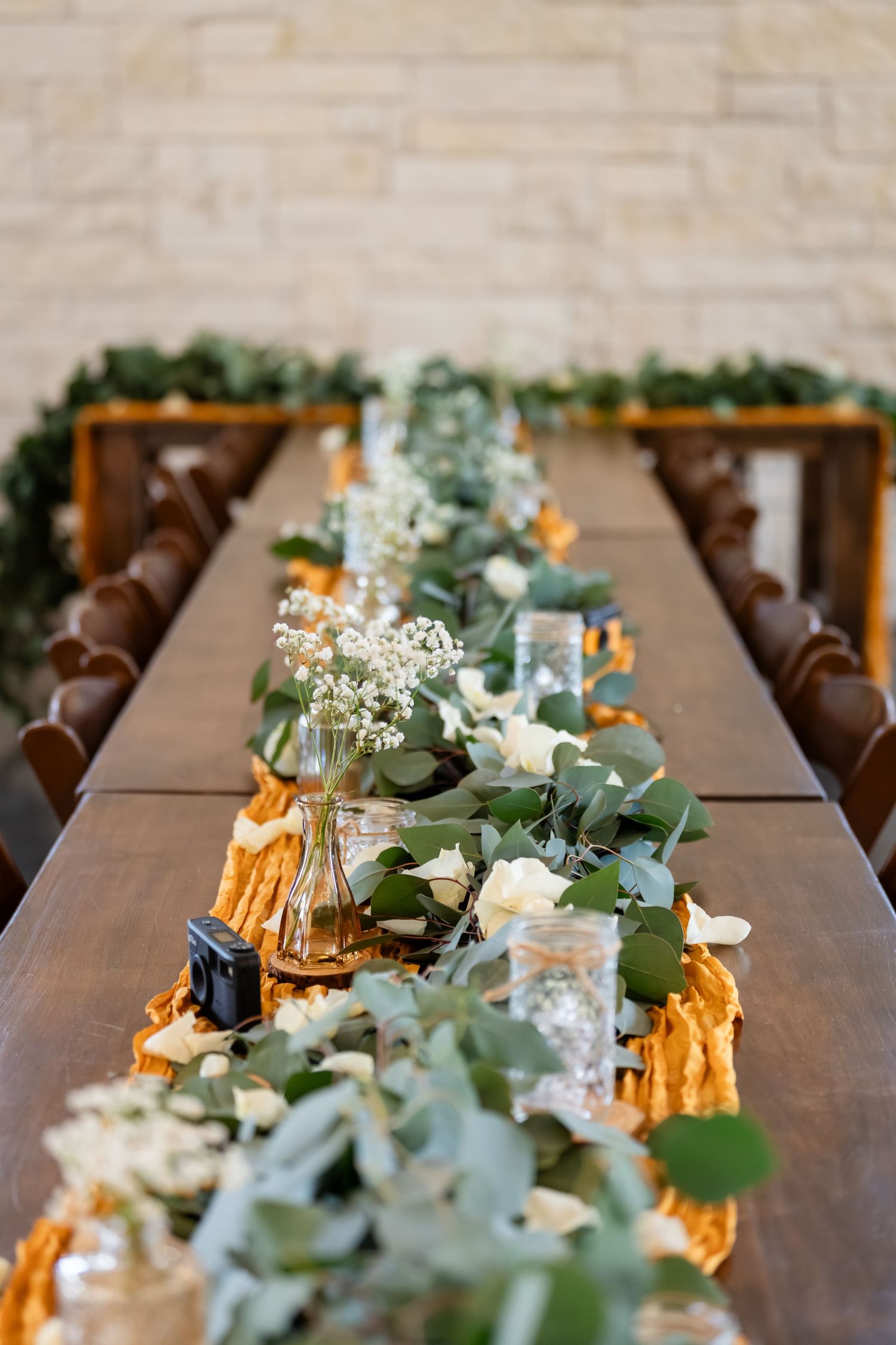 Elegant rustic wedding reception table with eucalyptus garland, white flowers, and golden runner on dark wood.