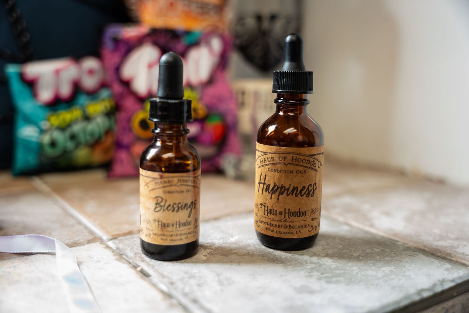 Two amber dropper bottles labeled Blessings and Happiness essential oils on a tile surface.