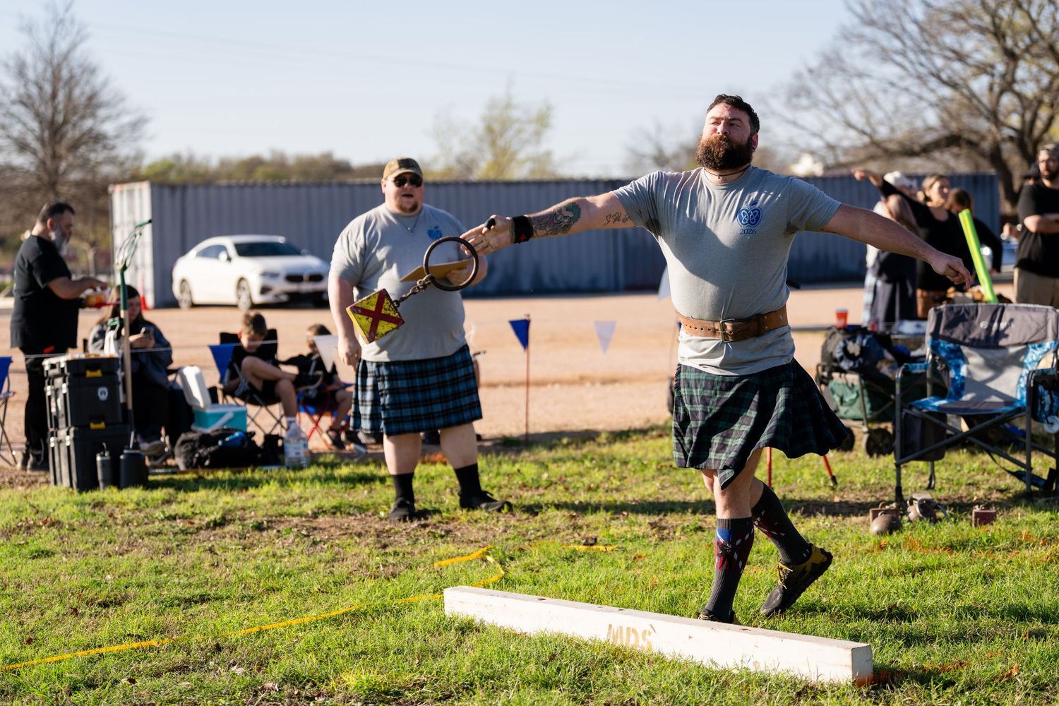 Man in kilt competing in Highland Games heavy athletics, throwing weight for distance outdoors.