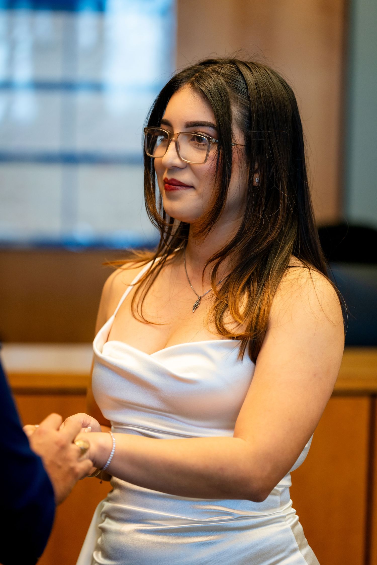 A person in a white sleeveless top sits indoors and gestures while speaking animatedly.