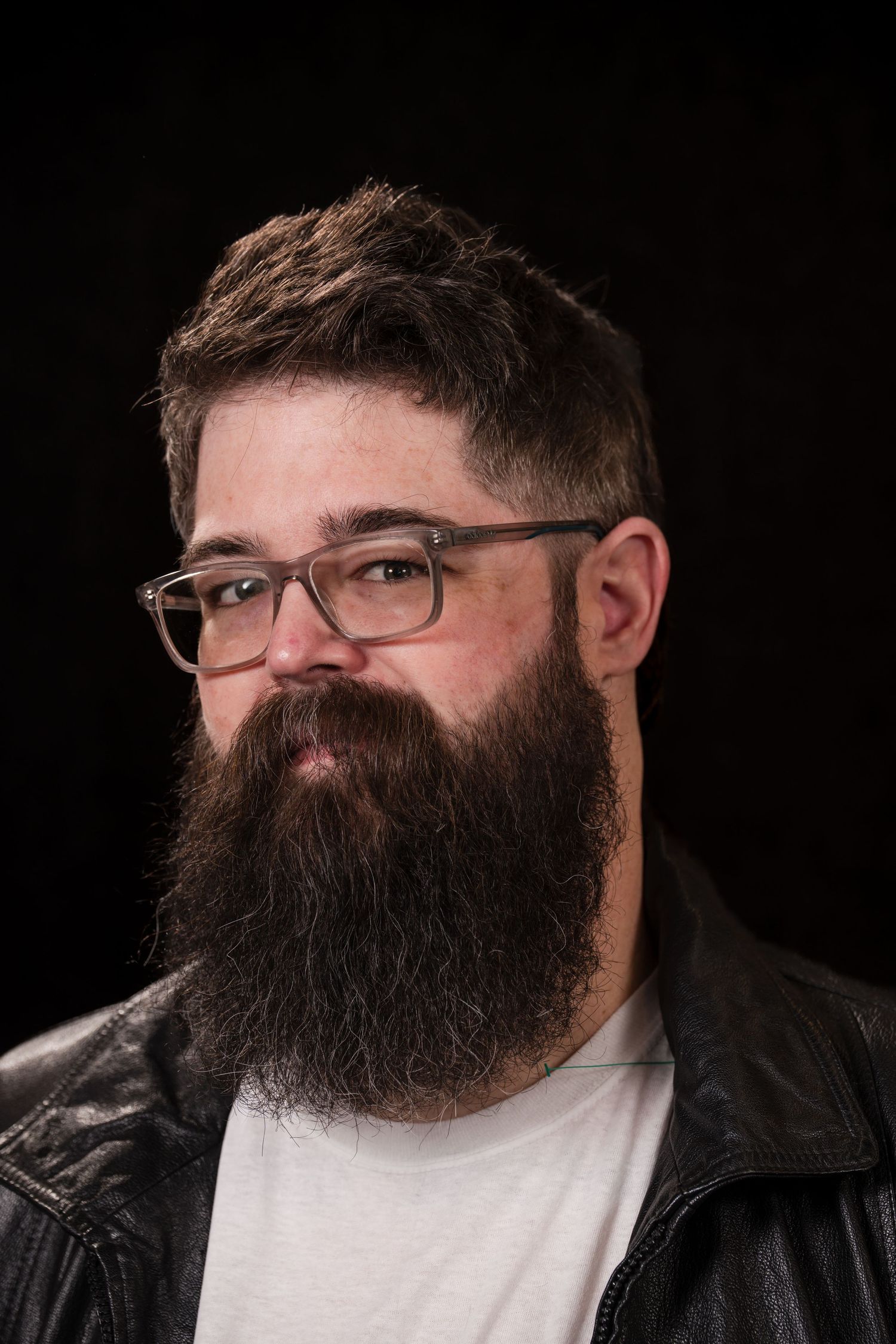 Profile shots of a person with a full dark beard and glasses wearing a black leather jacket against a black background.