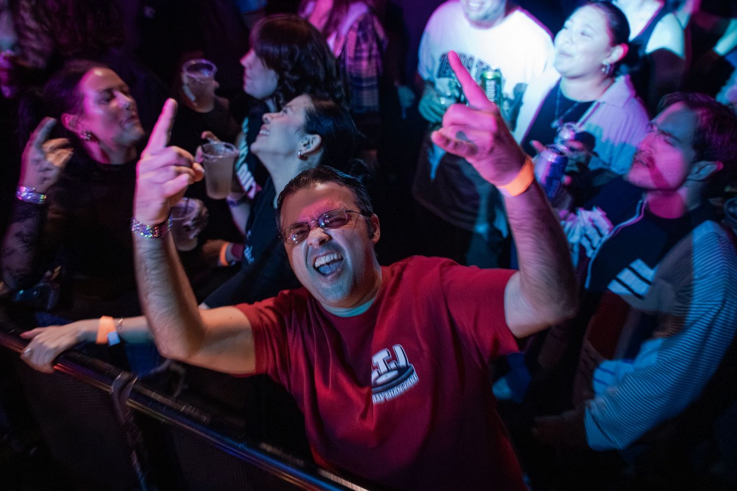 Concert crowd enjoying live music performance with colorful purple and blue lighting effects in a dark venue.