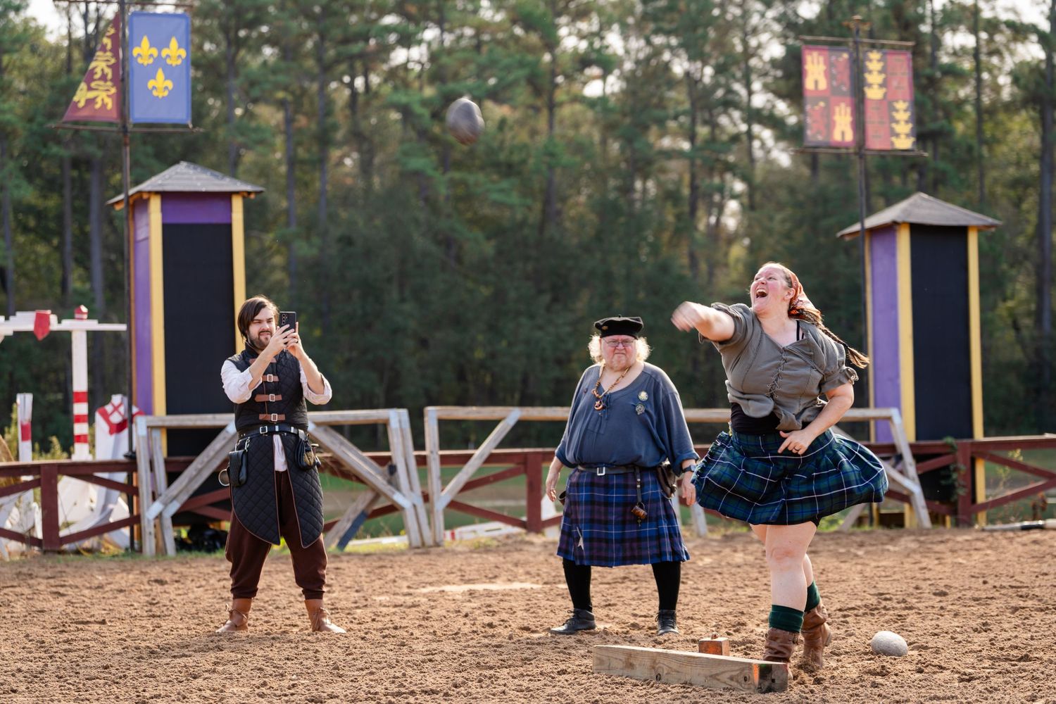 Performers in traditional Scottish and medieval costumes entertain visitors at a Renaissance festival grounds.