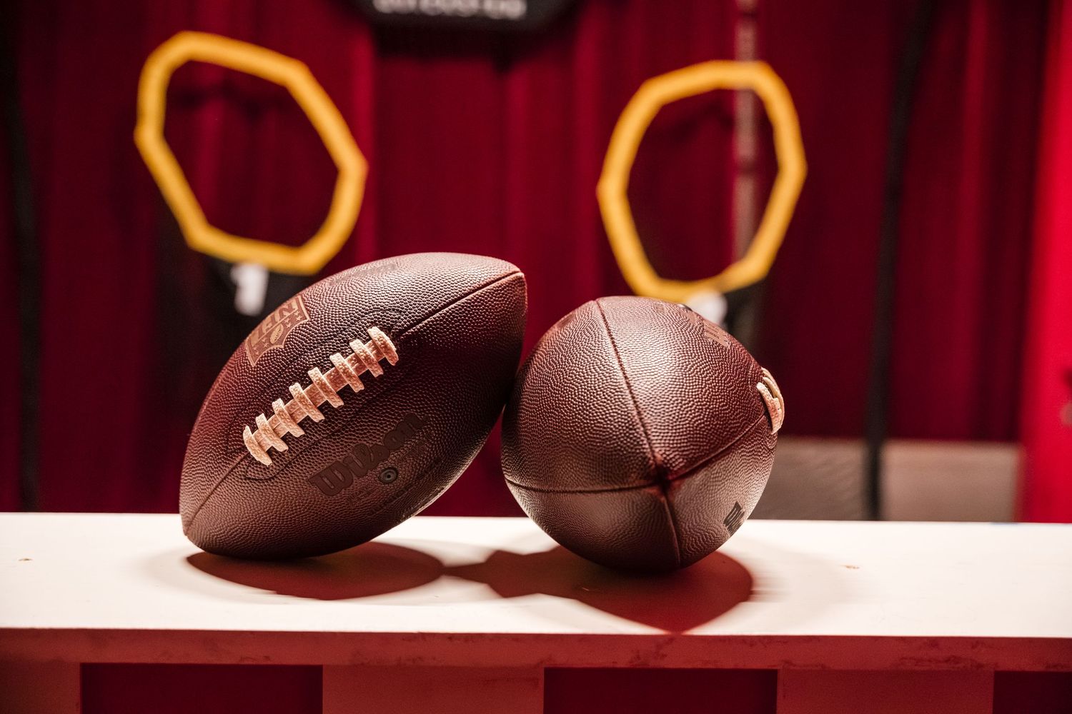 Multiple vintage brown leather footballs lined up against a red velvet backdrop in a display case.
