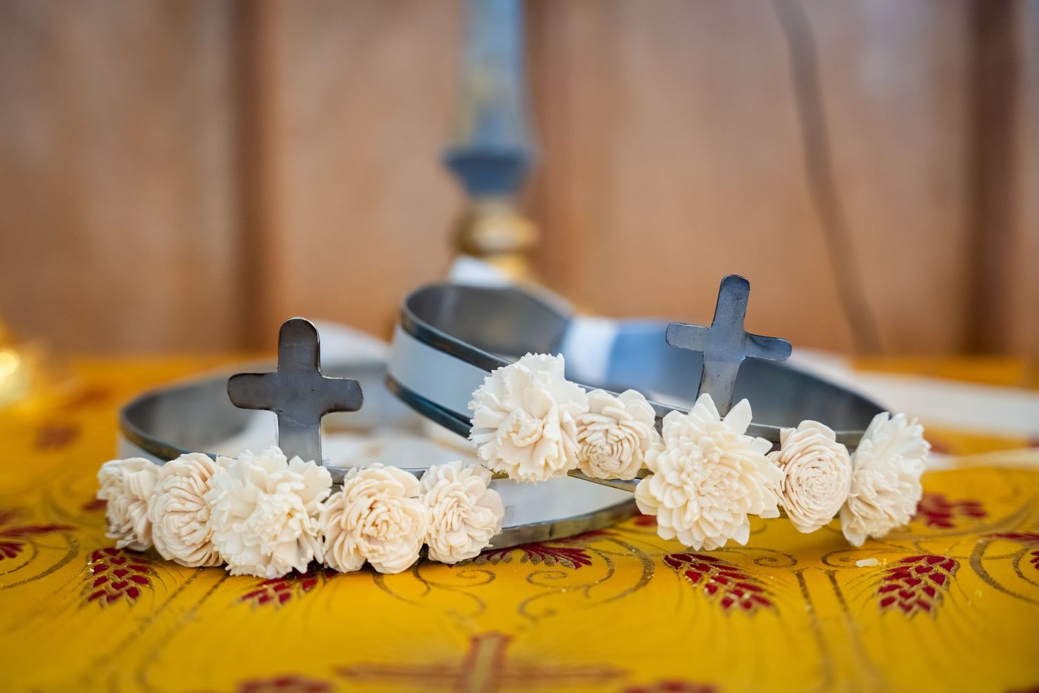 White carnation flowers arranged in a row with blue scissors on a yellow floral tablecloth.