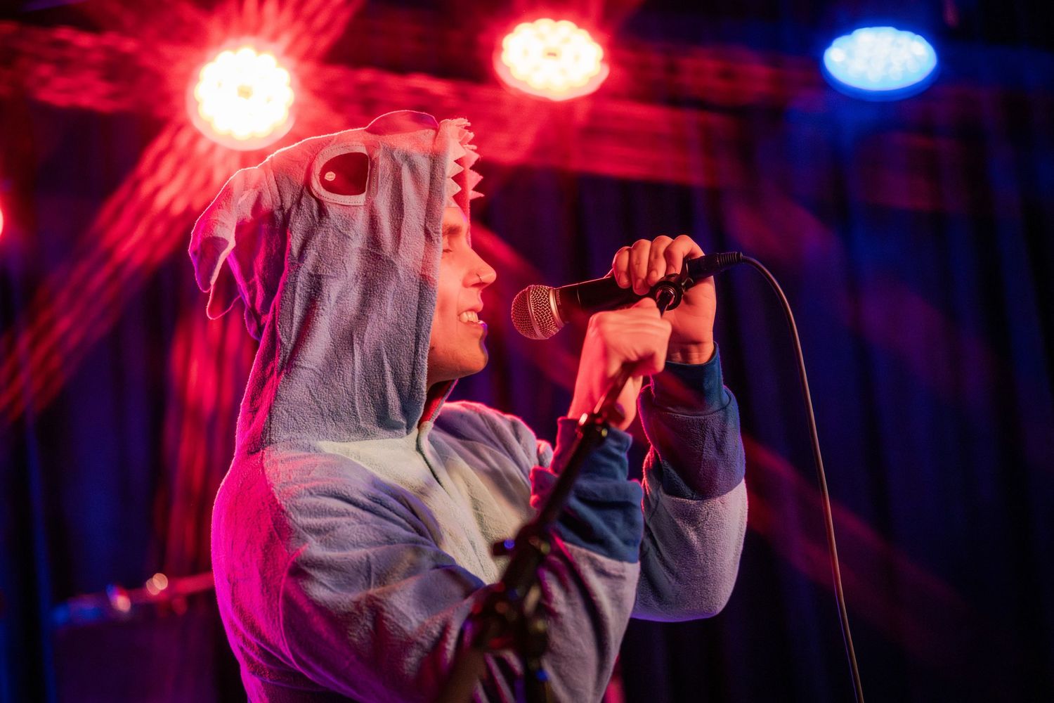Concert performer singing on stage illuminated by dramatic red and blue lighting effects during a live performance.
