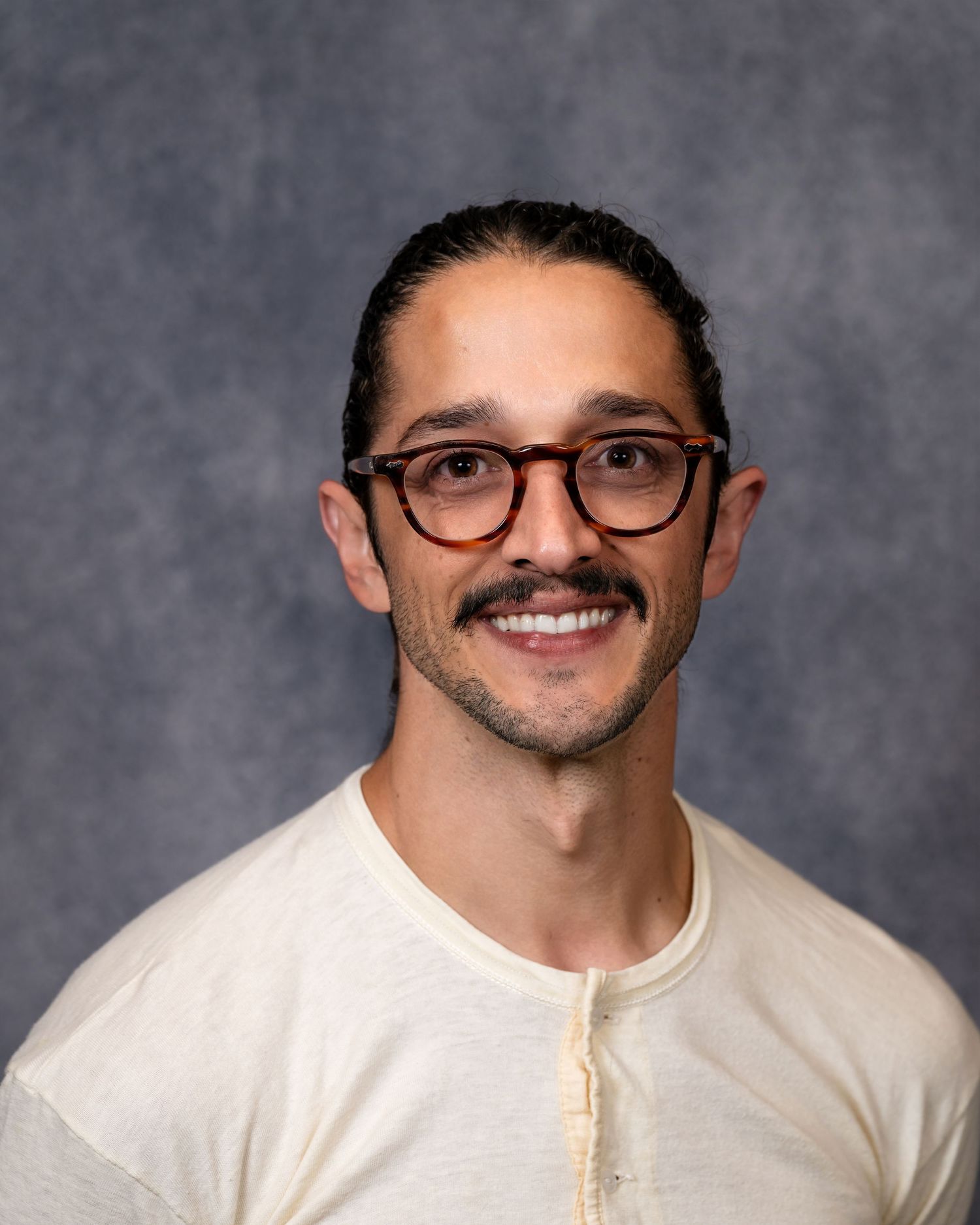 Professional headshot of a man with glasses, mustache, and dark hair wearing a cream henley shirt.