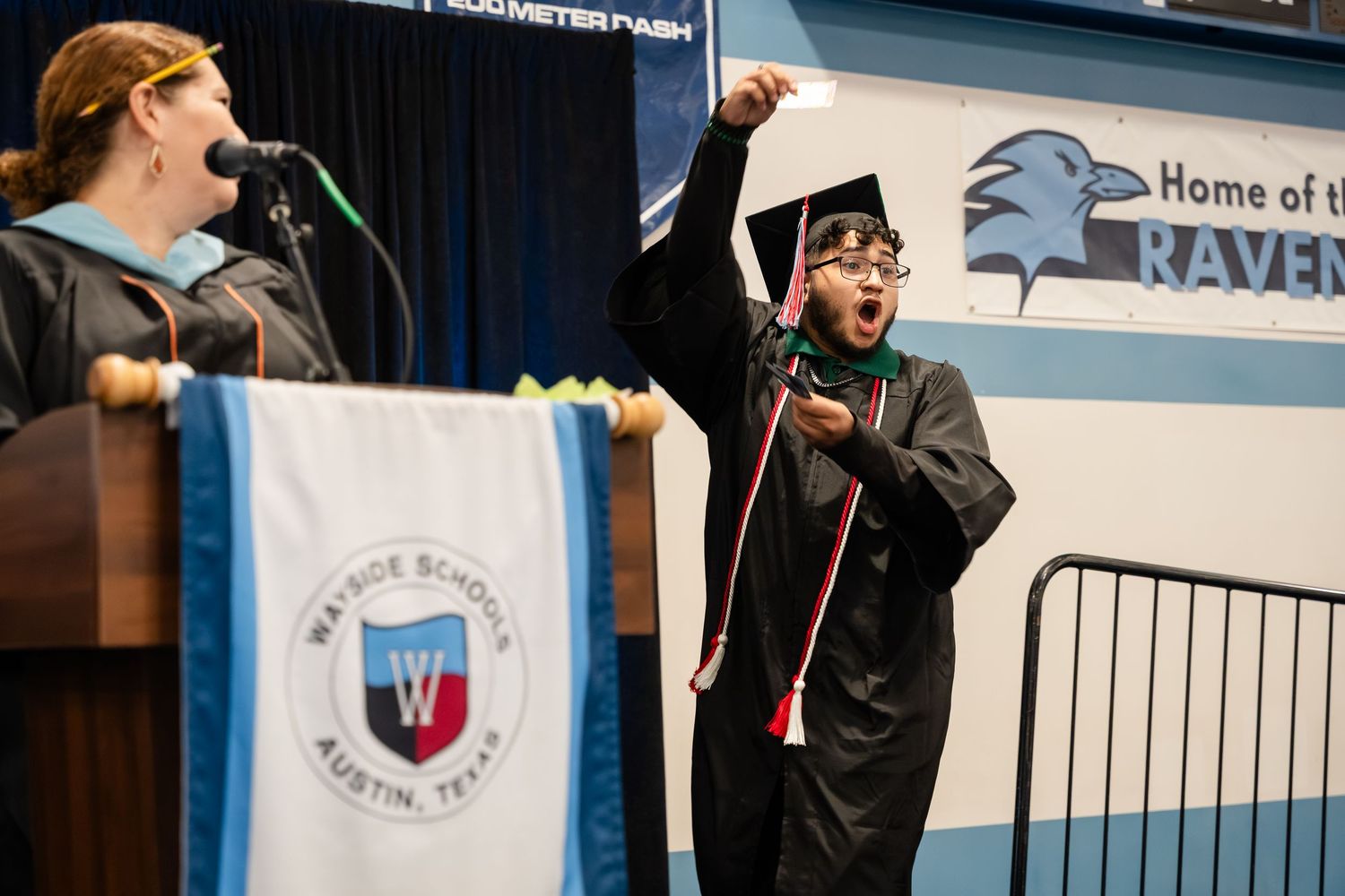 Excited graduate in cap and gown celebrates at Wayside School Austin Texas graduation ceremony on stage.