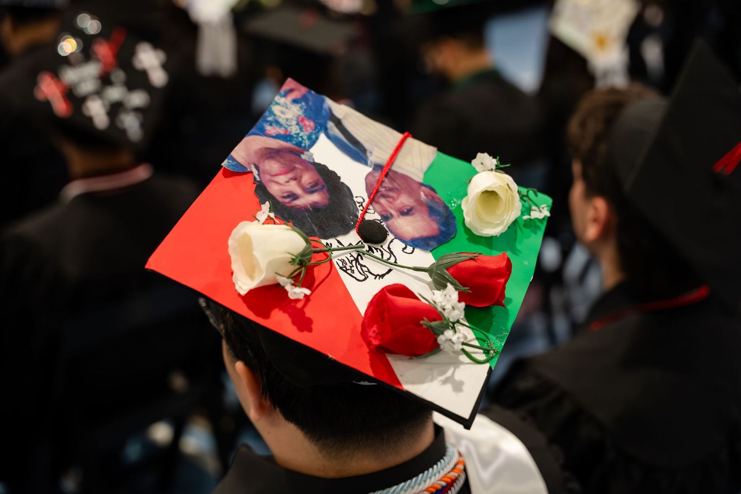 Decorated graduation cap with photos and red and white roses at a commencement ceremony.
