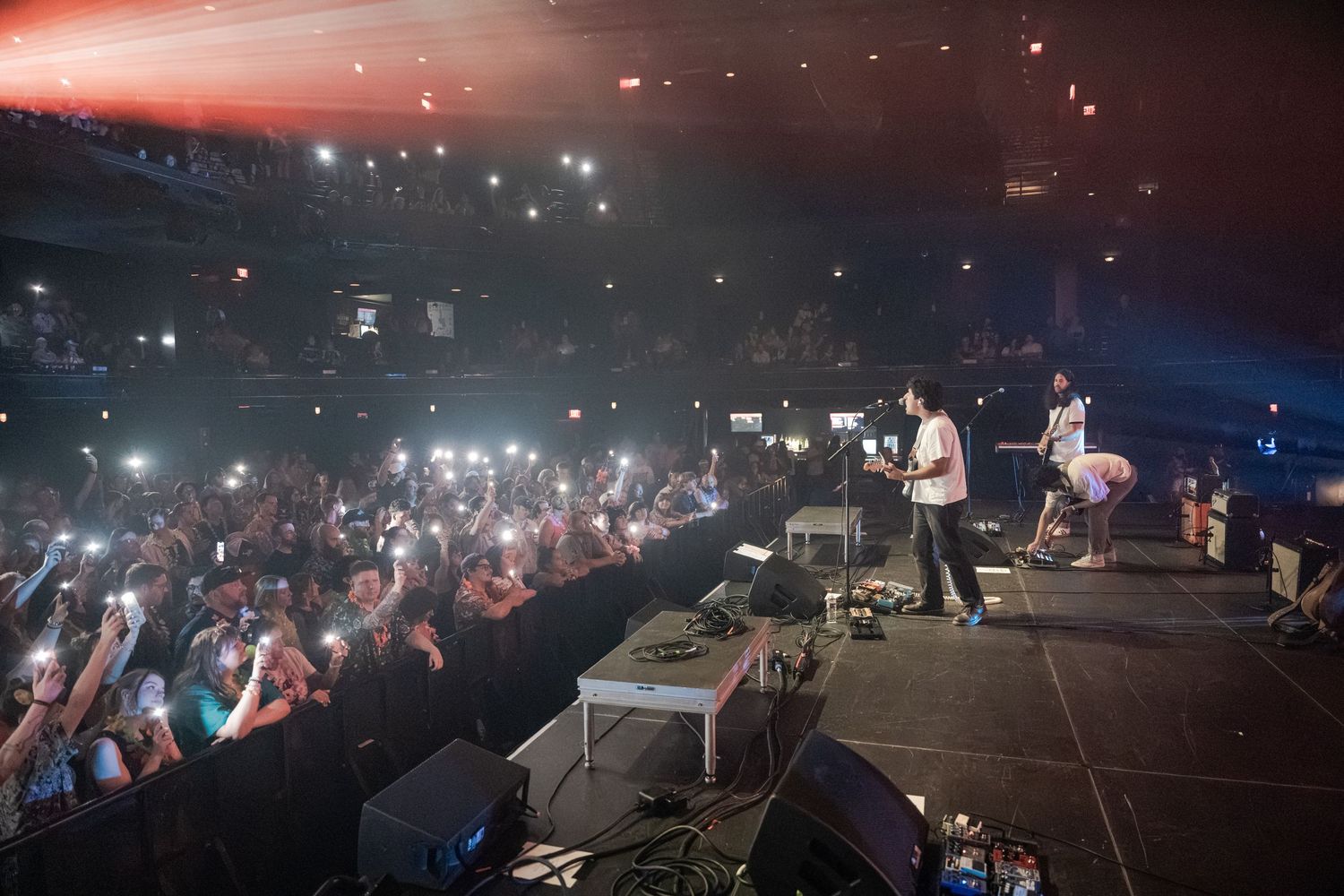 Live concert performance on stage with crowd holding up phone lights in a packed dark venue.