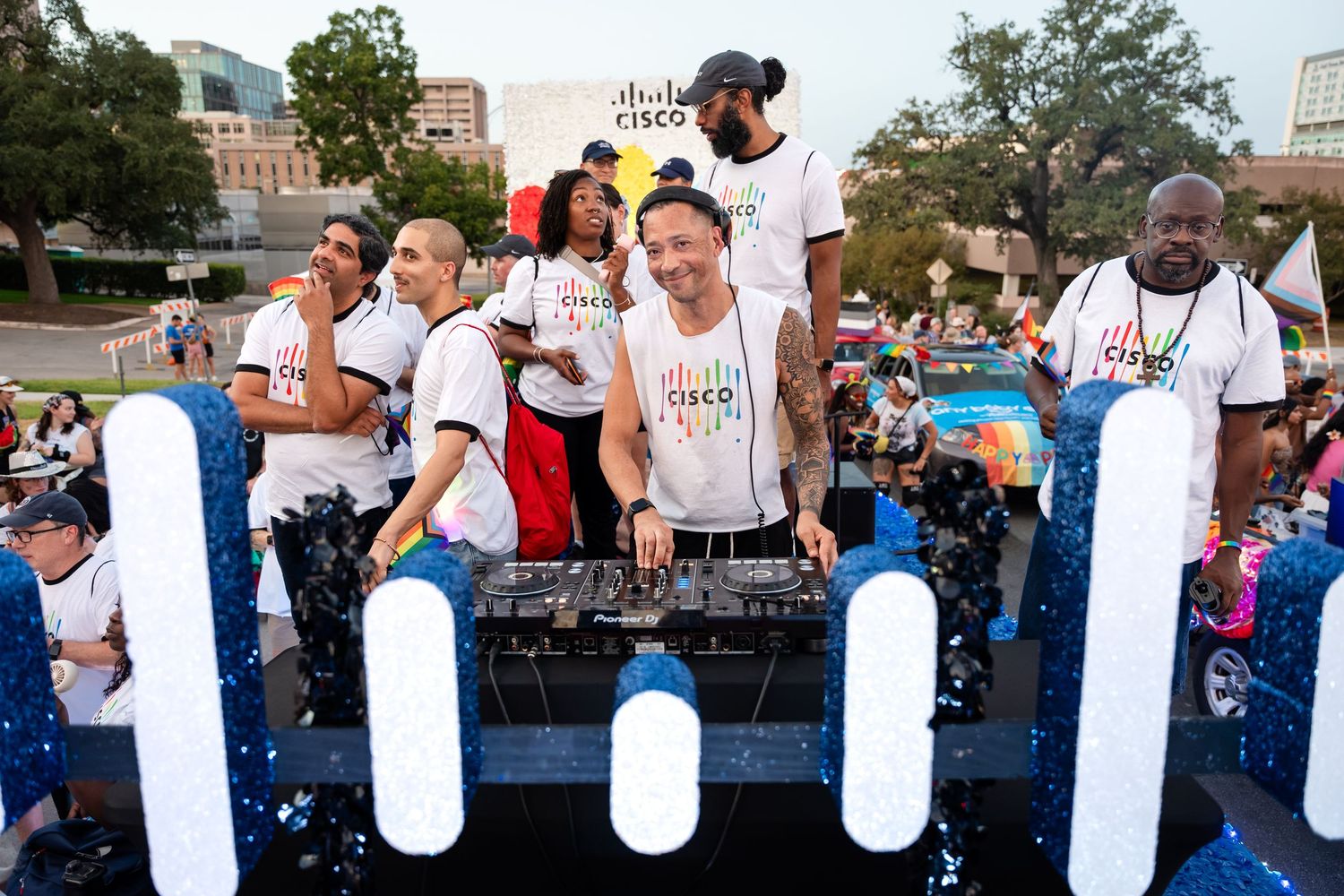 Cisco employees celebrate Pride on a festive parade float with a DJ and confetti at an outdoor event.