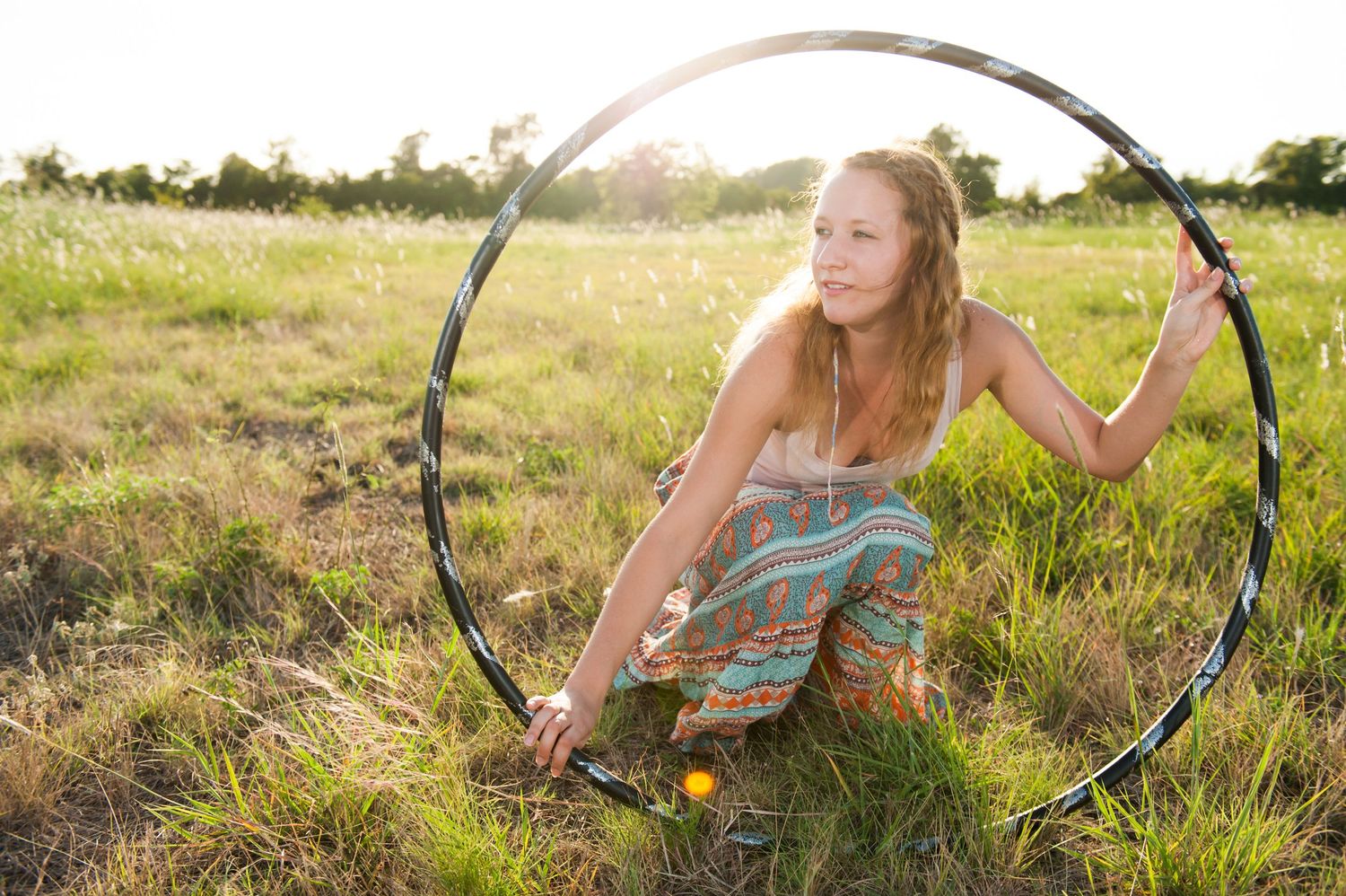 A person in a floral dress lies in a sunny meadow with tall grass and wildflowers during golden hour.