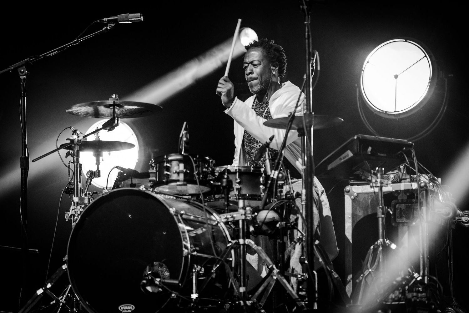 Dramatic black and white concert photography showing silhouettes of drummers performing on stage with dramatic lighting.