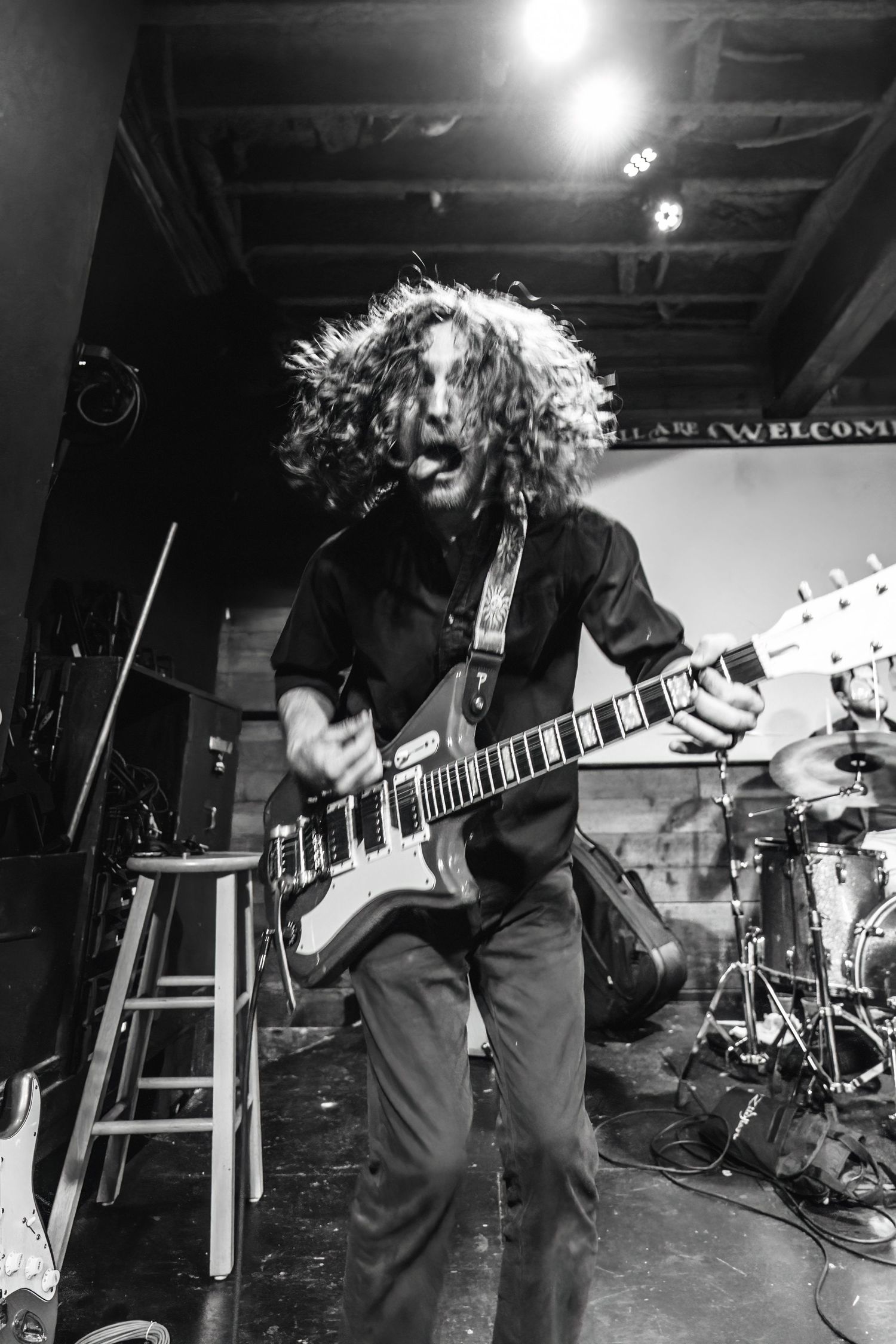 Guitarist performing on stage with energetic movements in a dimly lit venue during a rock concert.
