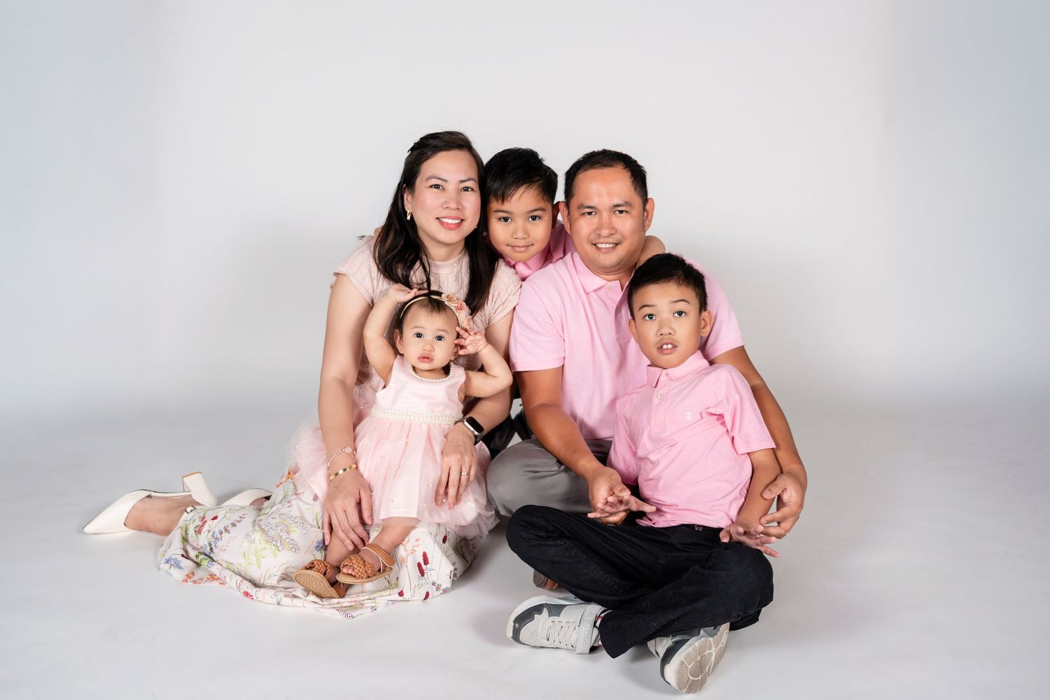 Happy Asian family of five posing together in matching pink outfits against a white studio background.