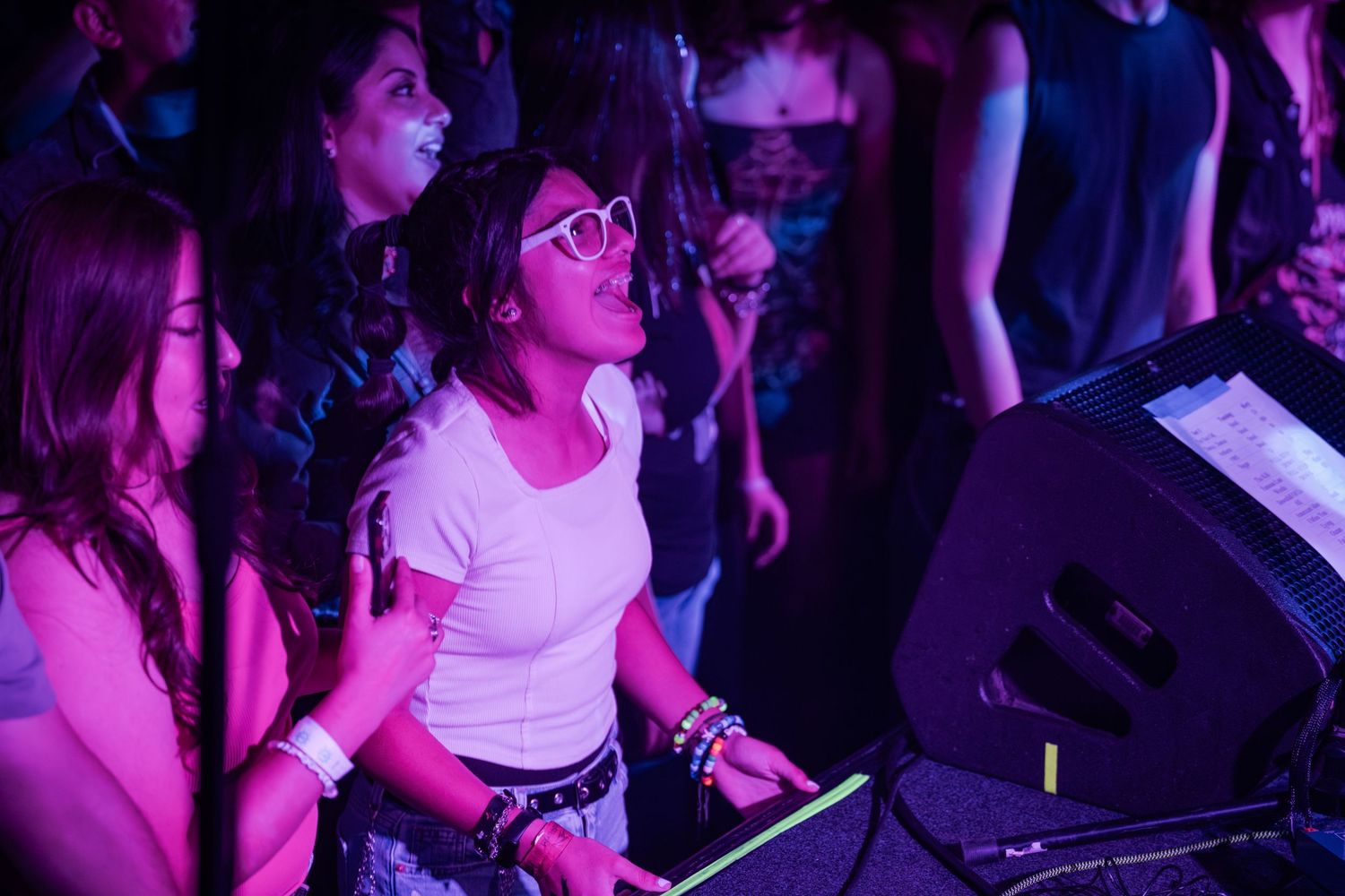 Young women dancing and enjoying music at a vibrant nightclub event with purple neon lights.