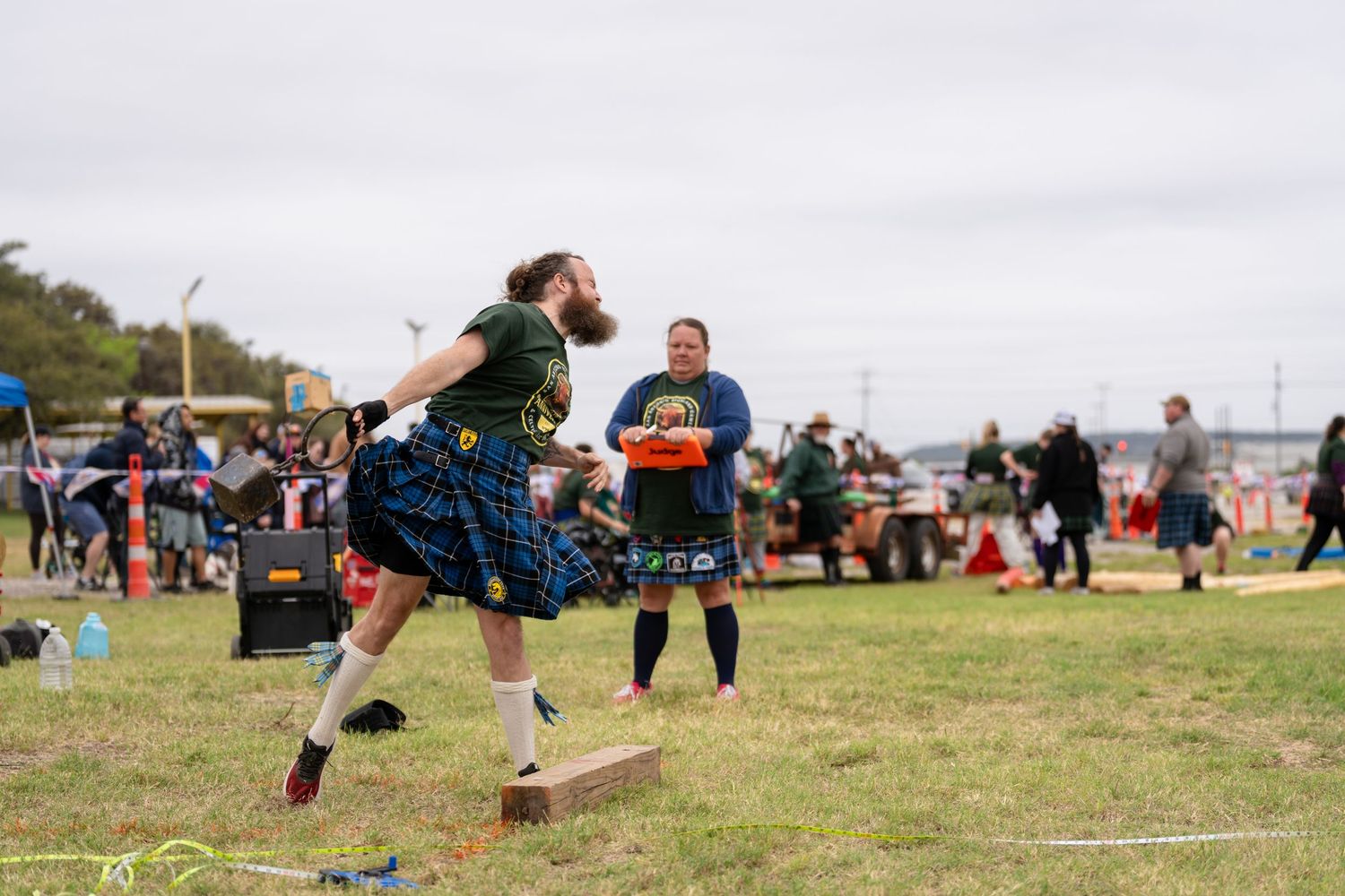 Man in Scottish kilt competes in Highland Games throwing event at outdoor festival with spectators watching.