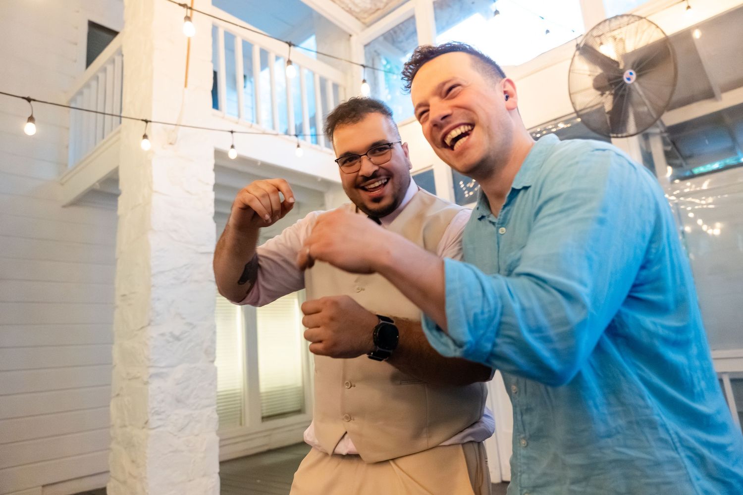 Two men laughing and flexing muscles together at an indoor celebration event.