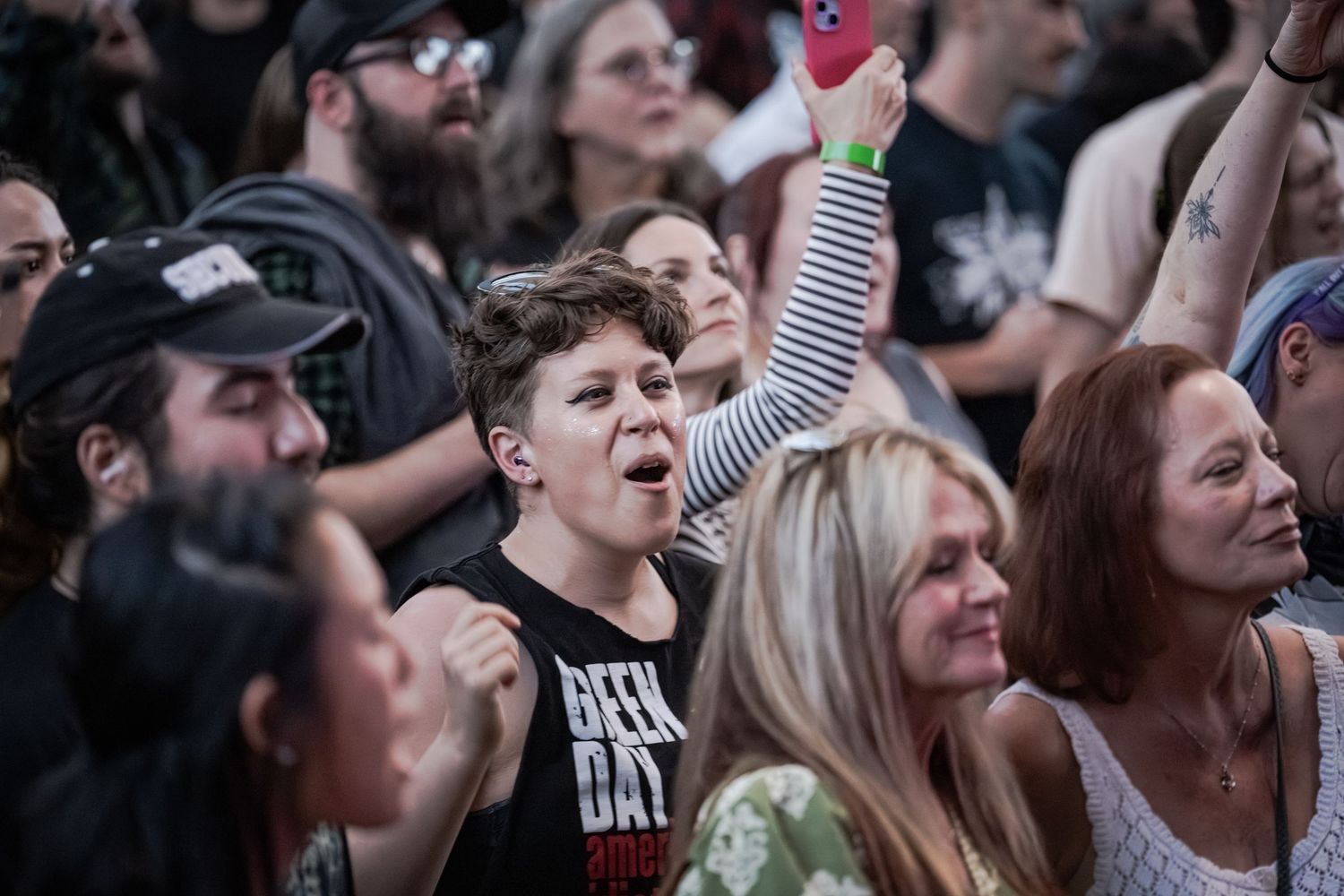 Excited young fan in Green Day shirt raises fist at outdoor rock concert amid cheering crowd.