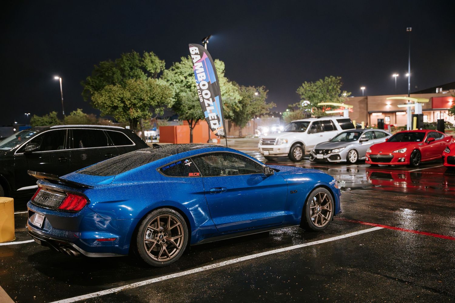 Modified blue Ford Mustang GT parked in a wet parking lot at night.