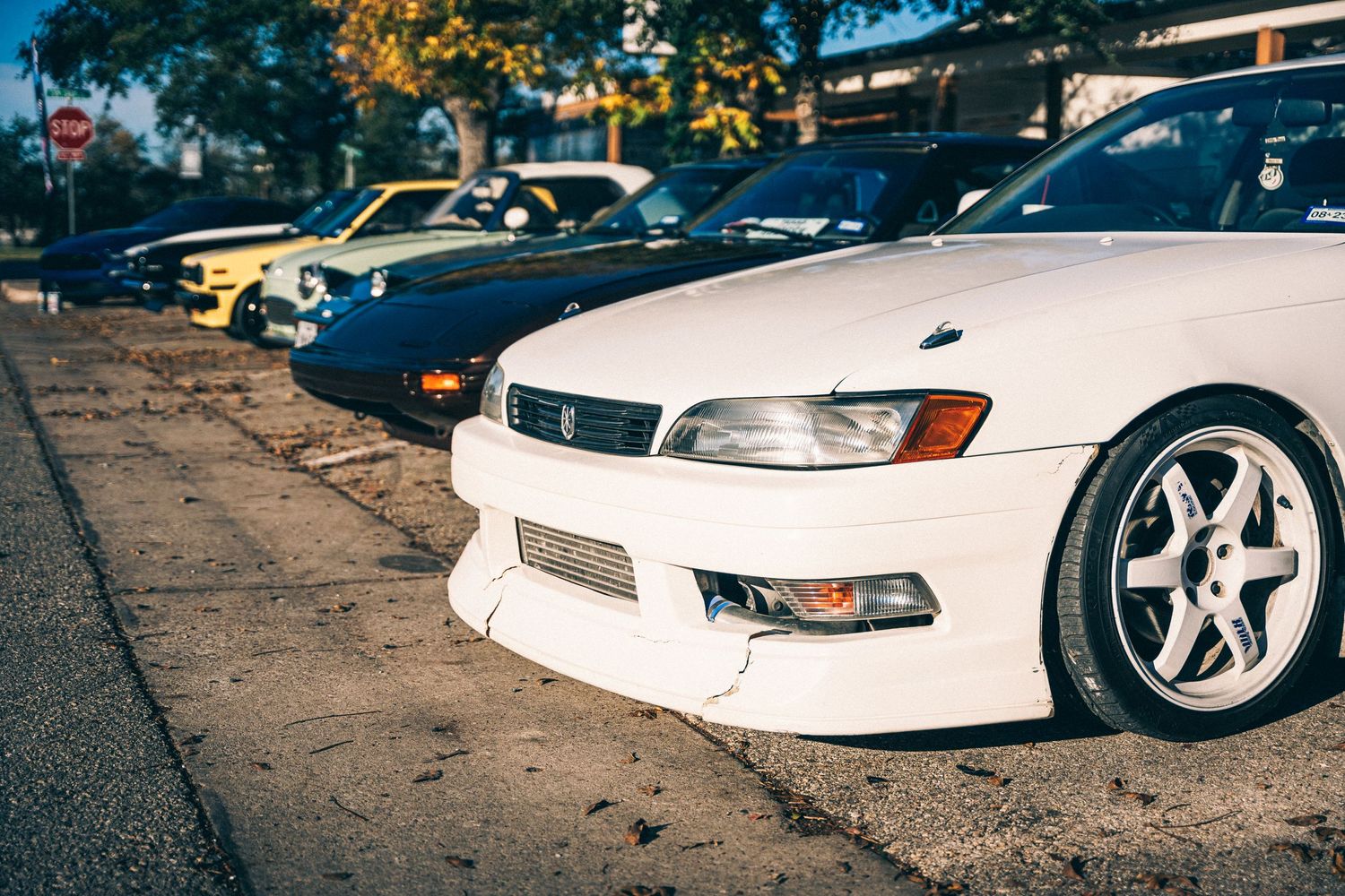 Modified white Toyota Mark II JZX100 with aftermarket wheels parked on street.
