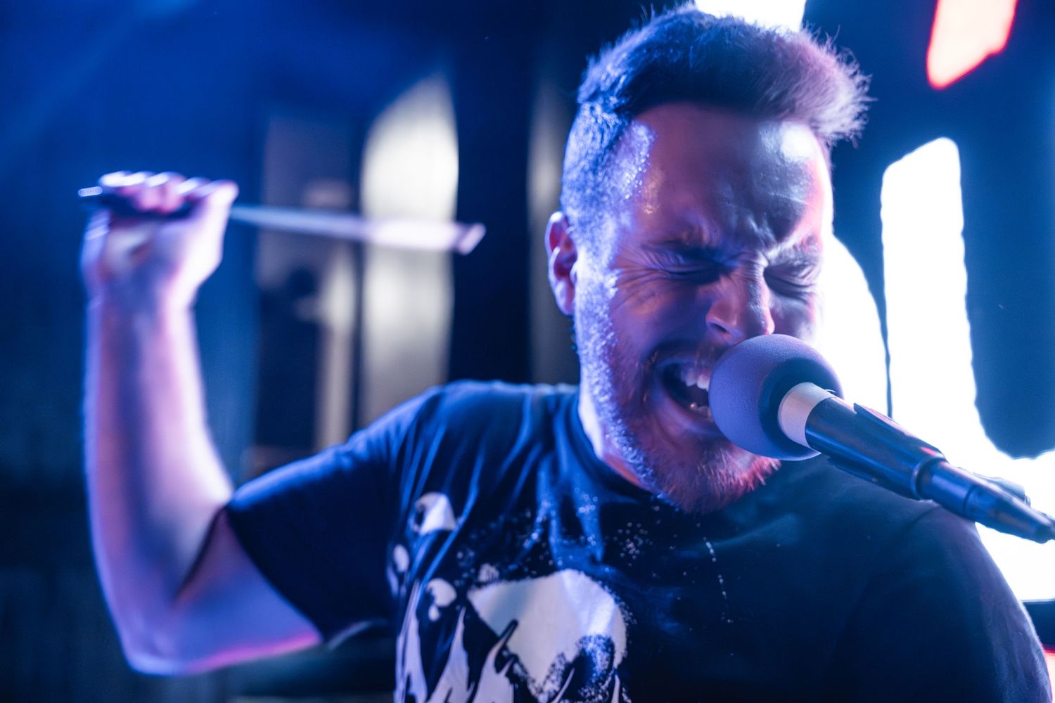 Rock vocalist passionately singing into microphone during energetic stage performance.