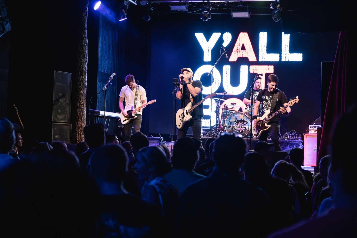 Band performs on stage with illuminated signage while crowd watches from below.