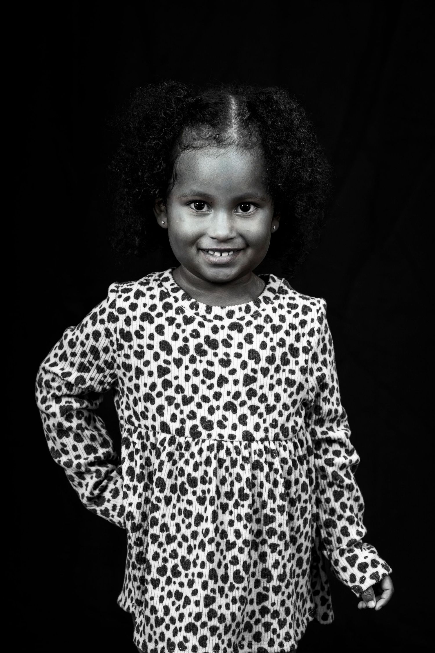 Child wearing leopard print dress smiles brightly in black and white portrait photo.
