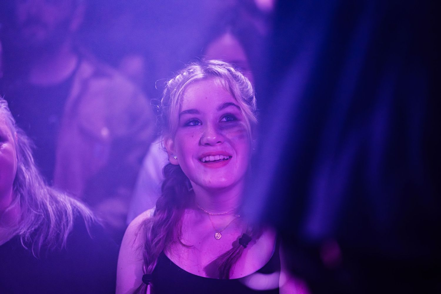 Young woman smiling and enjoying a concert in purple lighting atmosphere.