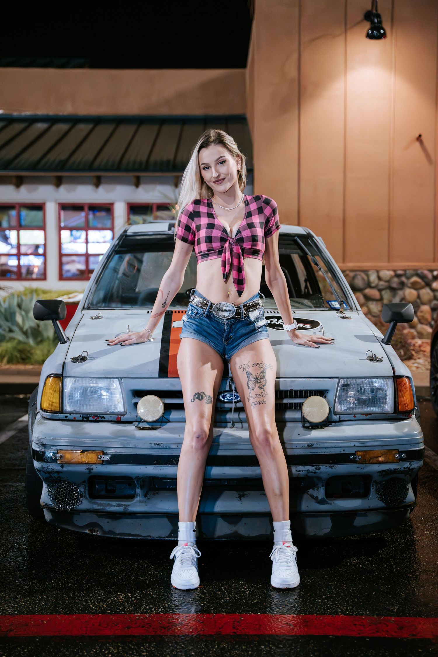 Casual street fashion pose on the hood of a silver car at night.