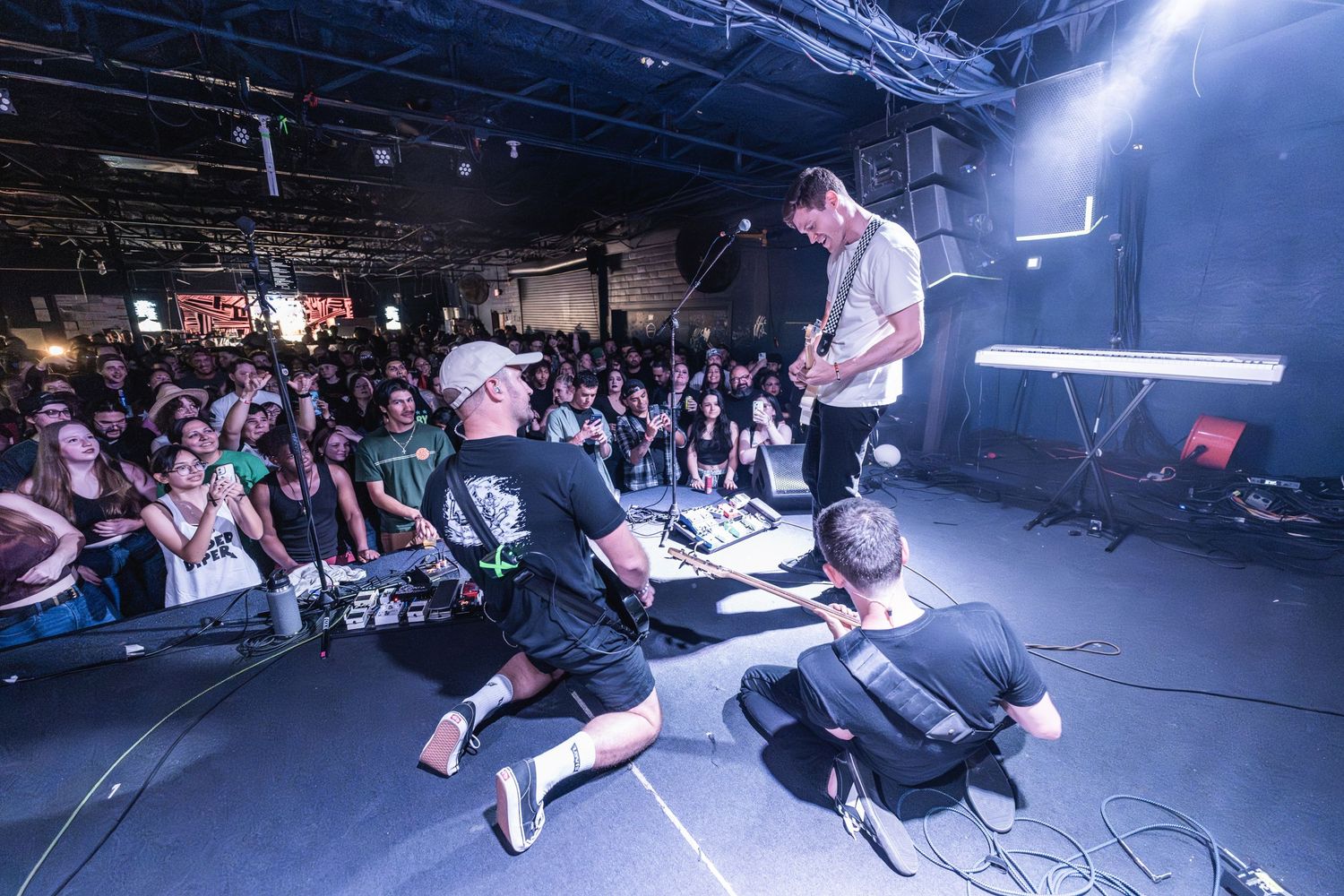 Musicians perform on stage for an enthusiastic crowd in a packed venue.