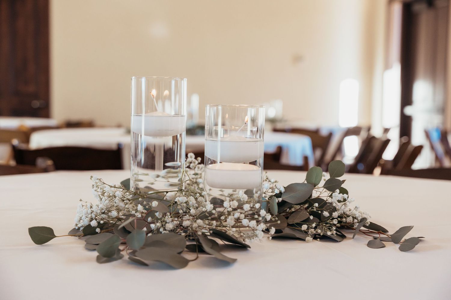 Wedding reception centerpiece with white candles and eucalyptus leaves on round table.