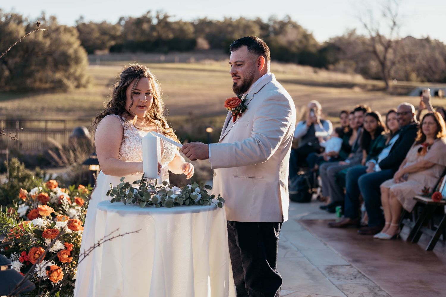 Couple performs unity ceremony ritual at outdoor wedding with floral decorations.