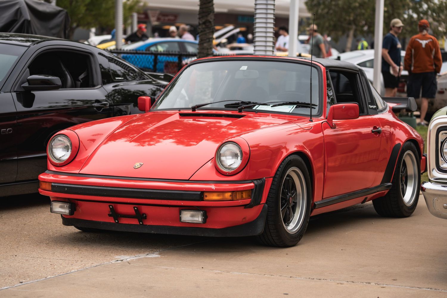Classic red Porsche 911 with black Fuchs wheels displayed at an outdoor auto meet.