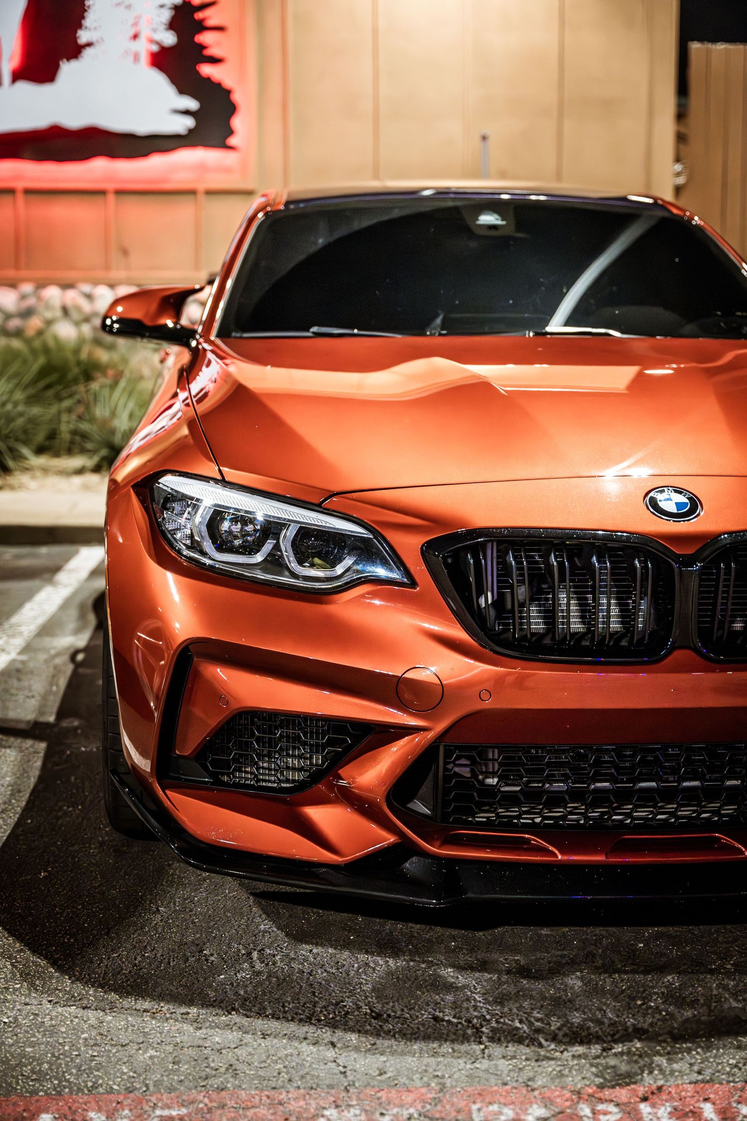 Close up of an orange BMW M2 Competition front end showing aggressive grill and LED headlights.