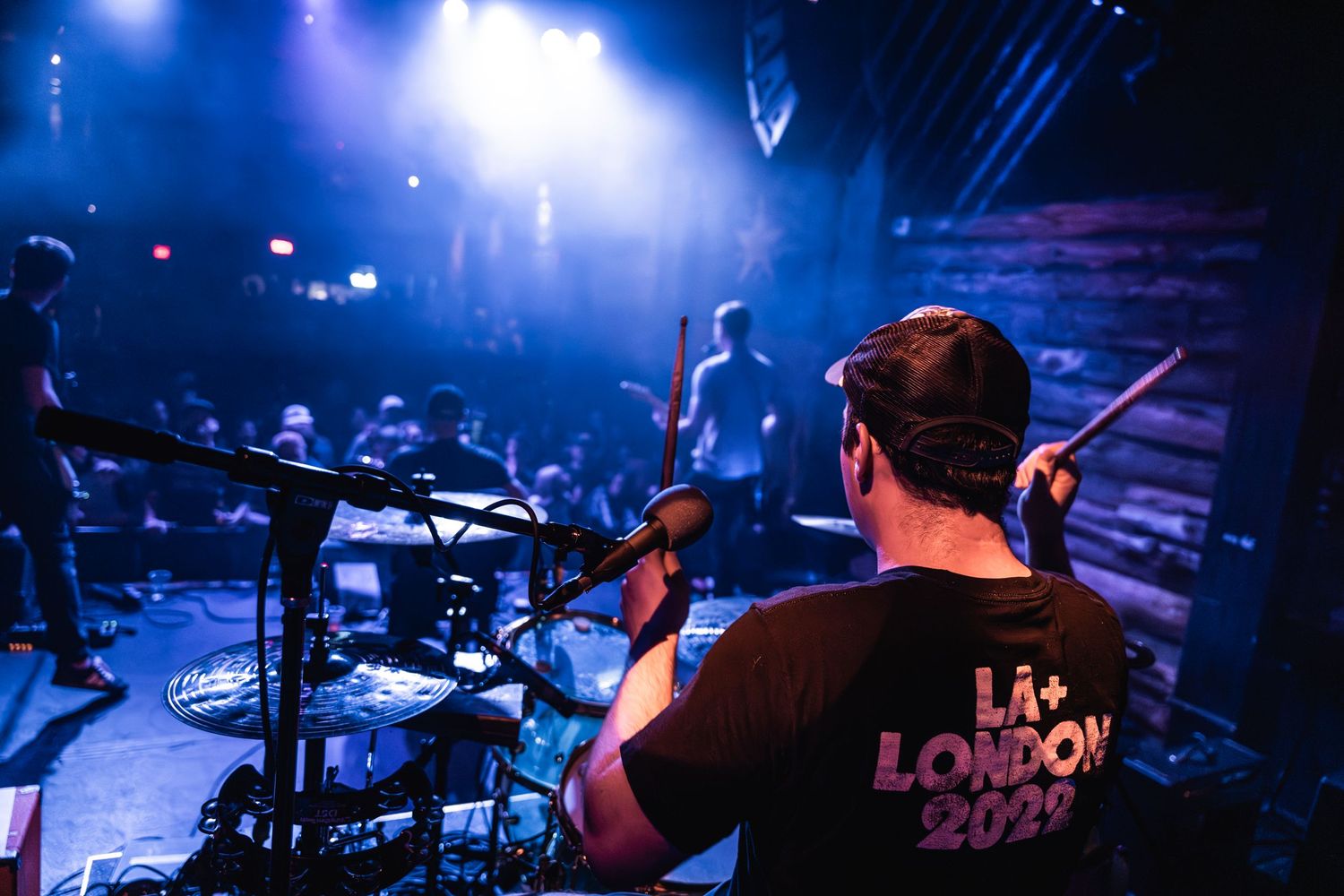 Drummer performing on stage with blue lighting effects and drum kit.