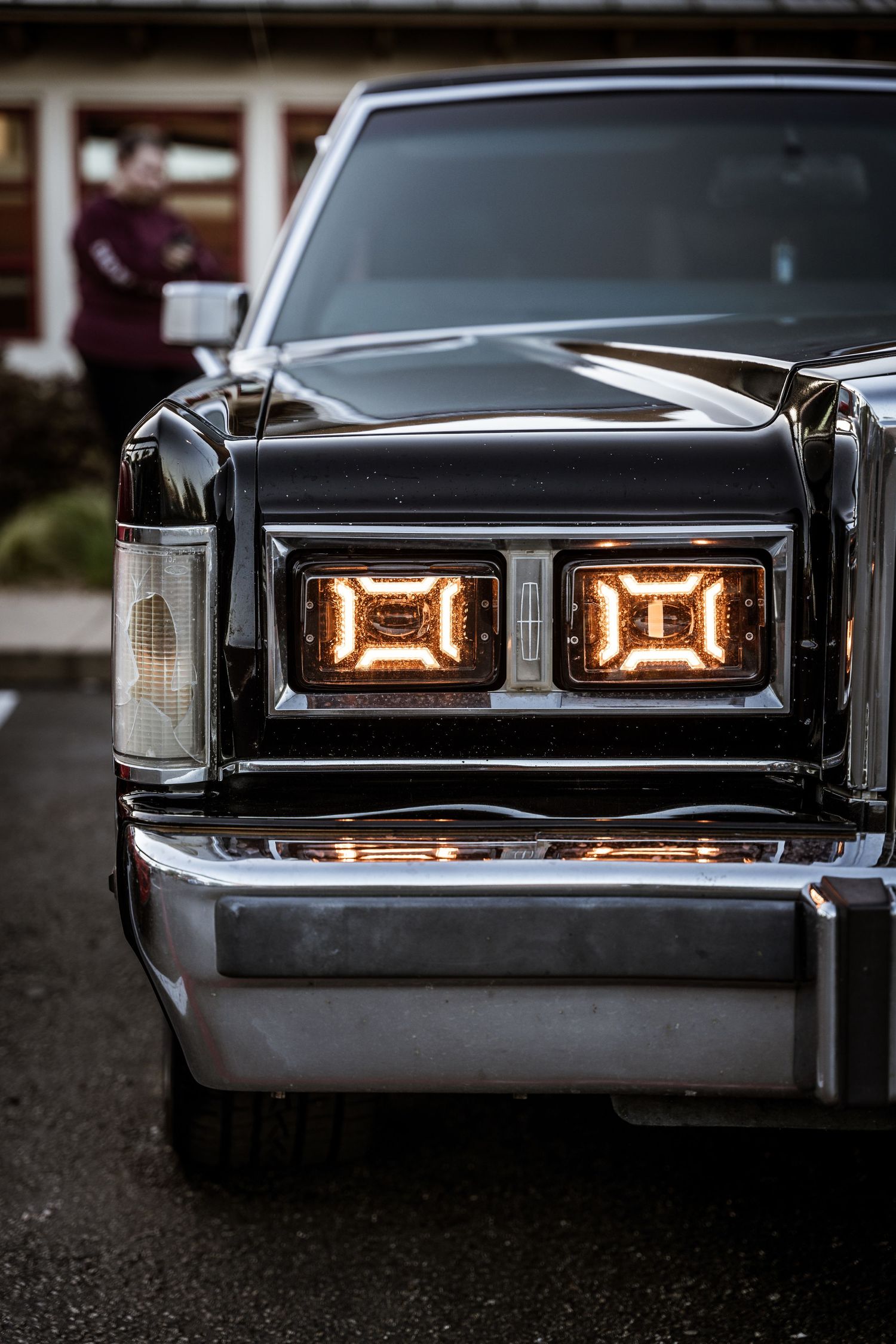 Front view of a classic Lincoln showing retro square headlights illuminated at dusk.