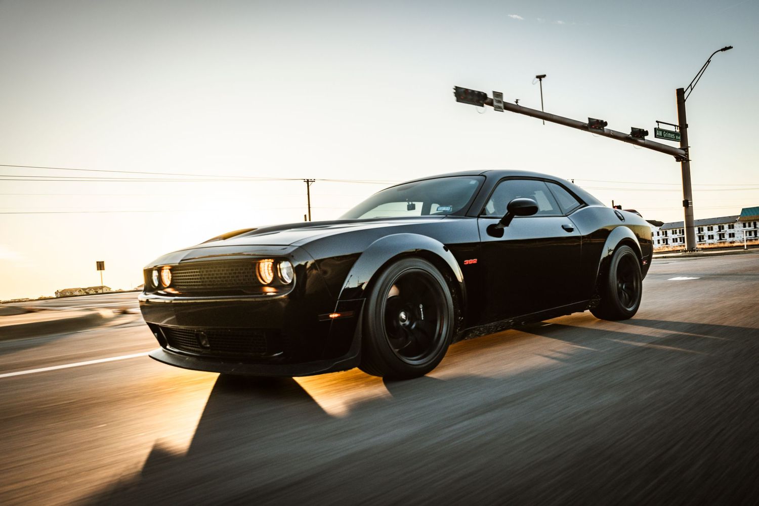 Menacing black Dodge Challenger with wide body kit photographed in motion at dusk.