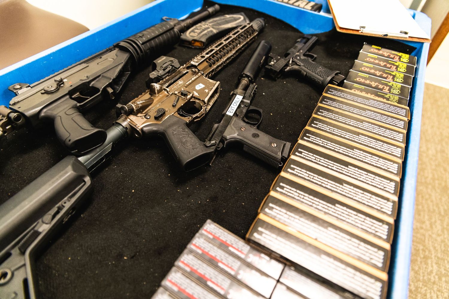 Display case containing tactical rifles and ammunition magazines on black fabric.