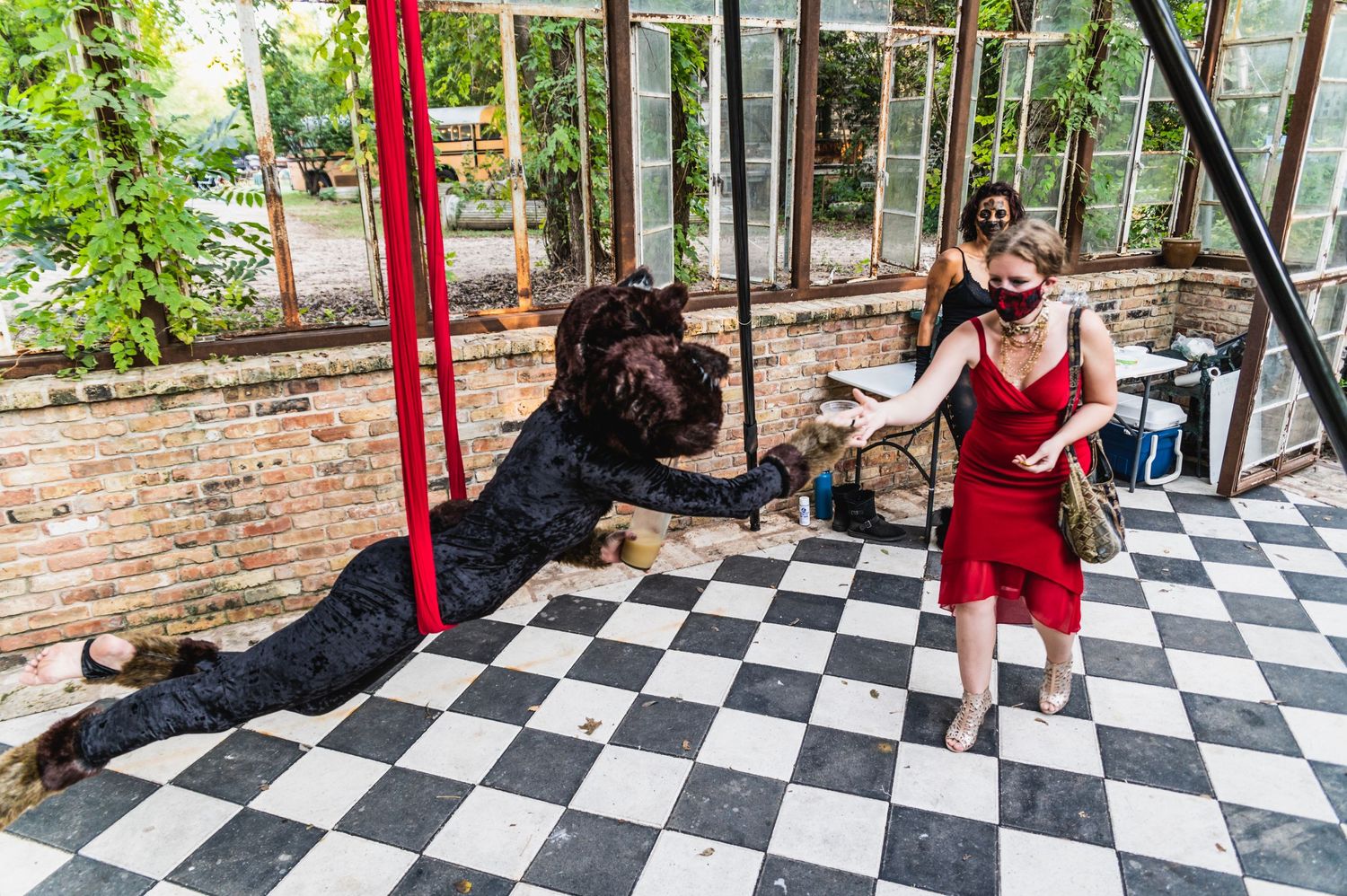 Two performers practice aerial silks choreography on checkered floor in brick-walled studio.
