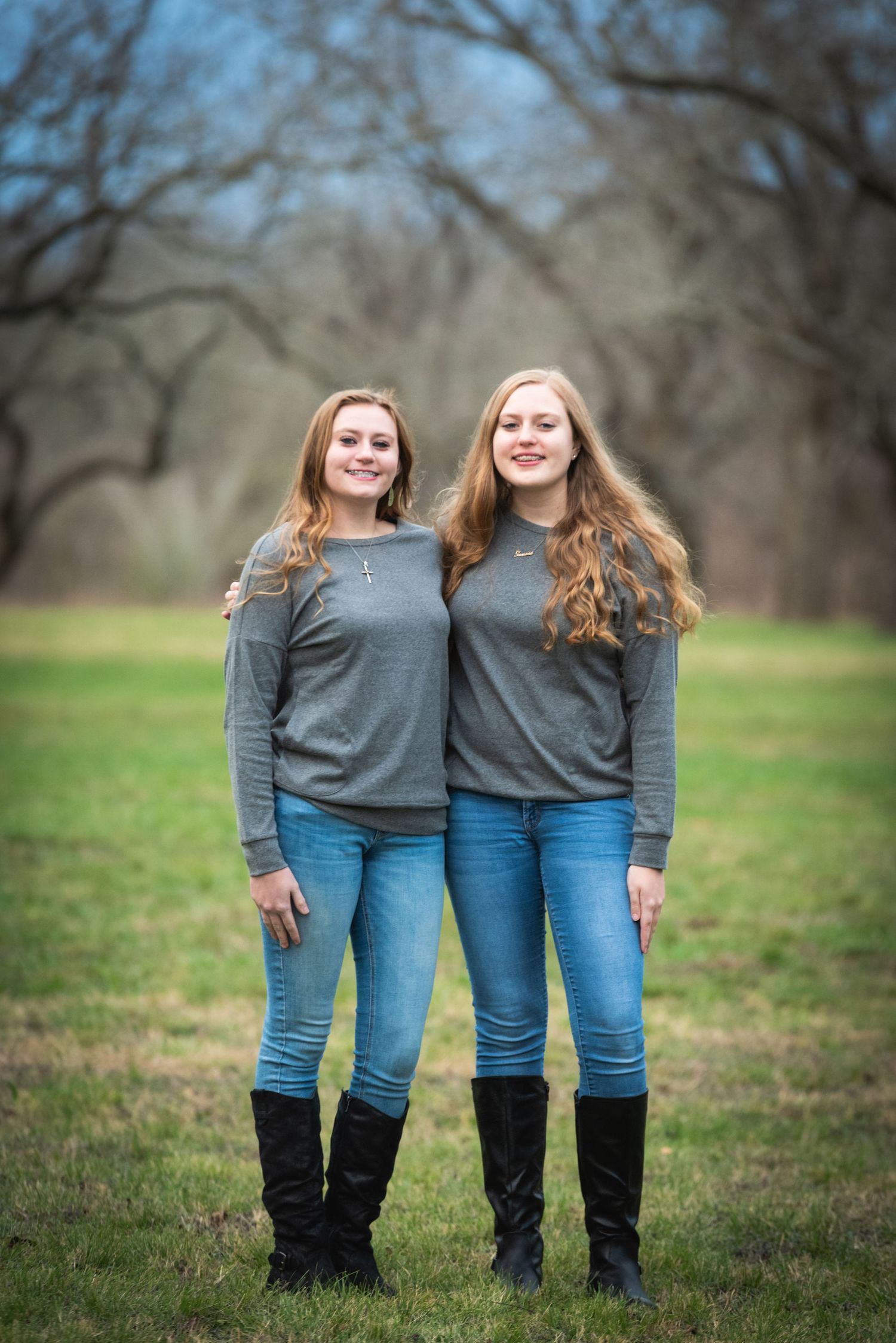 Two people in matching gray sweaters and jeans stand together outdoors.